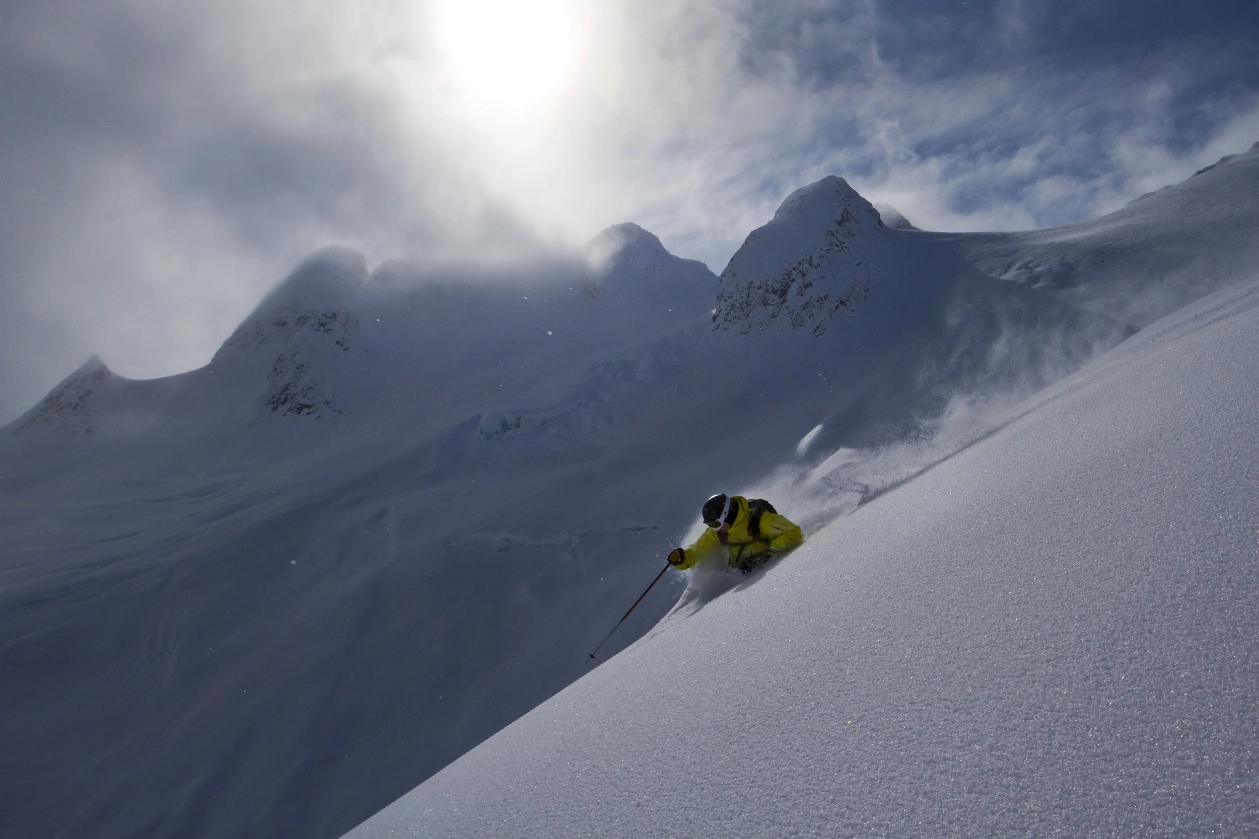 Skier pole planting in deep alpine powder with snow-covered mountains and sunlight in the background