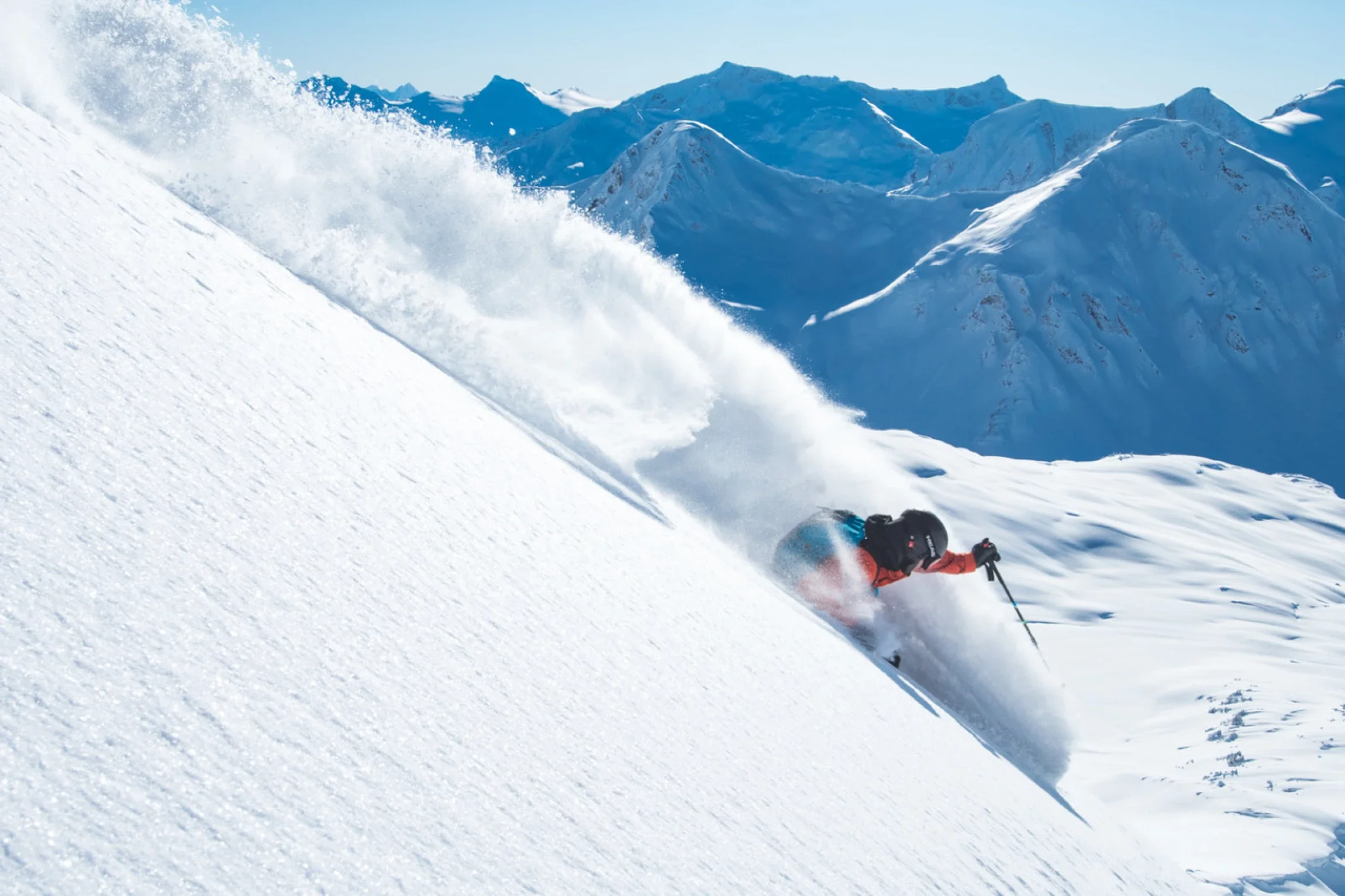 Skier making a big powder slash in the alpine with snow-covered mountains behind at northern escape terrace bc