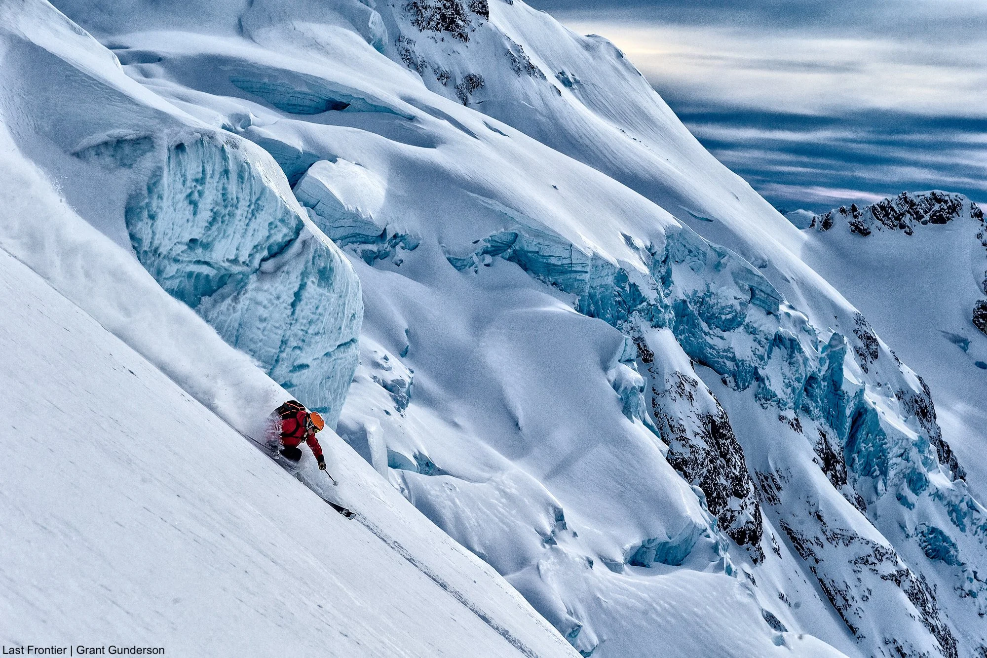 Skier descending through deep snow with a broken glacier and steep alpine terrain behind.
