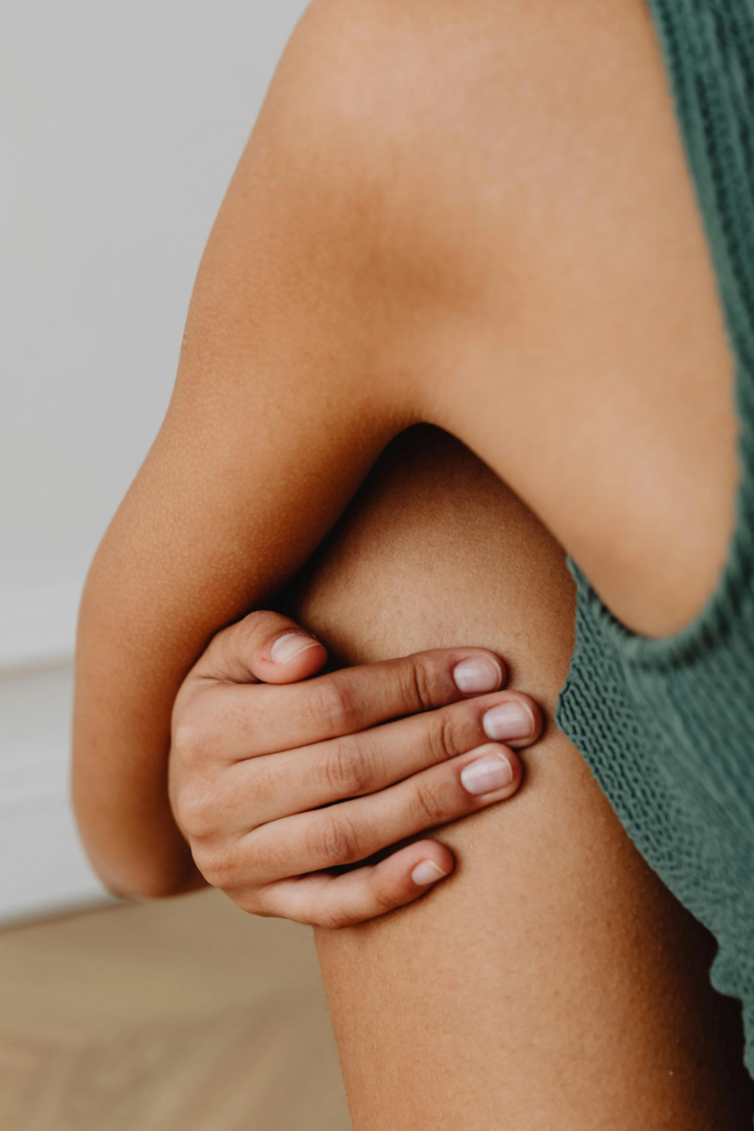 Mains tenant la peau d'une jambe nue, avec un vêtement vert sur le côté.