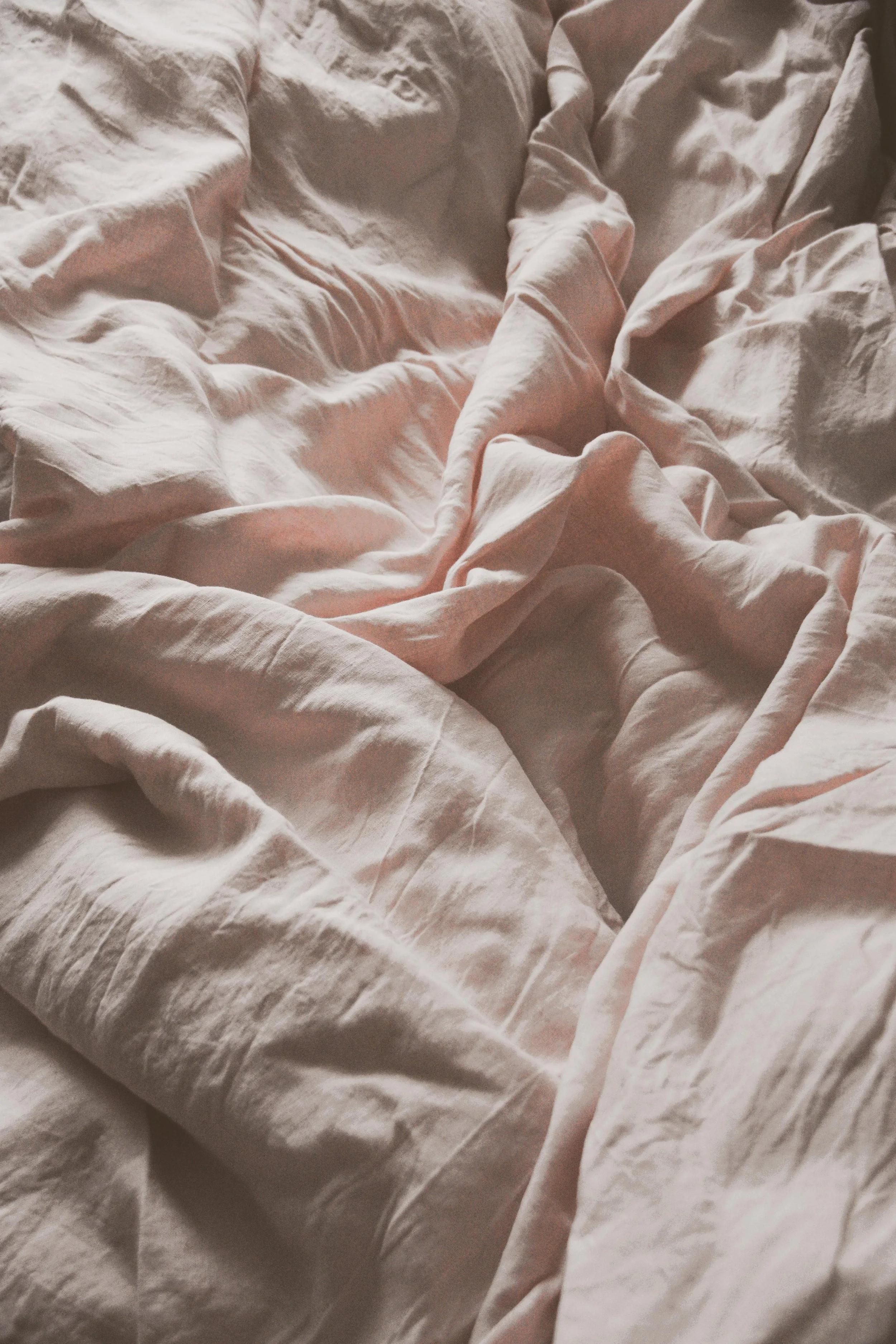 Lits en désordre avec des draps en coton beige ou blanc, légèrement froissés.