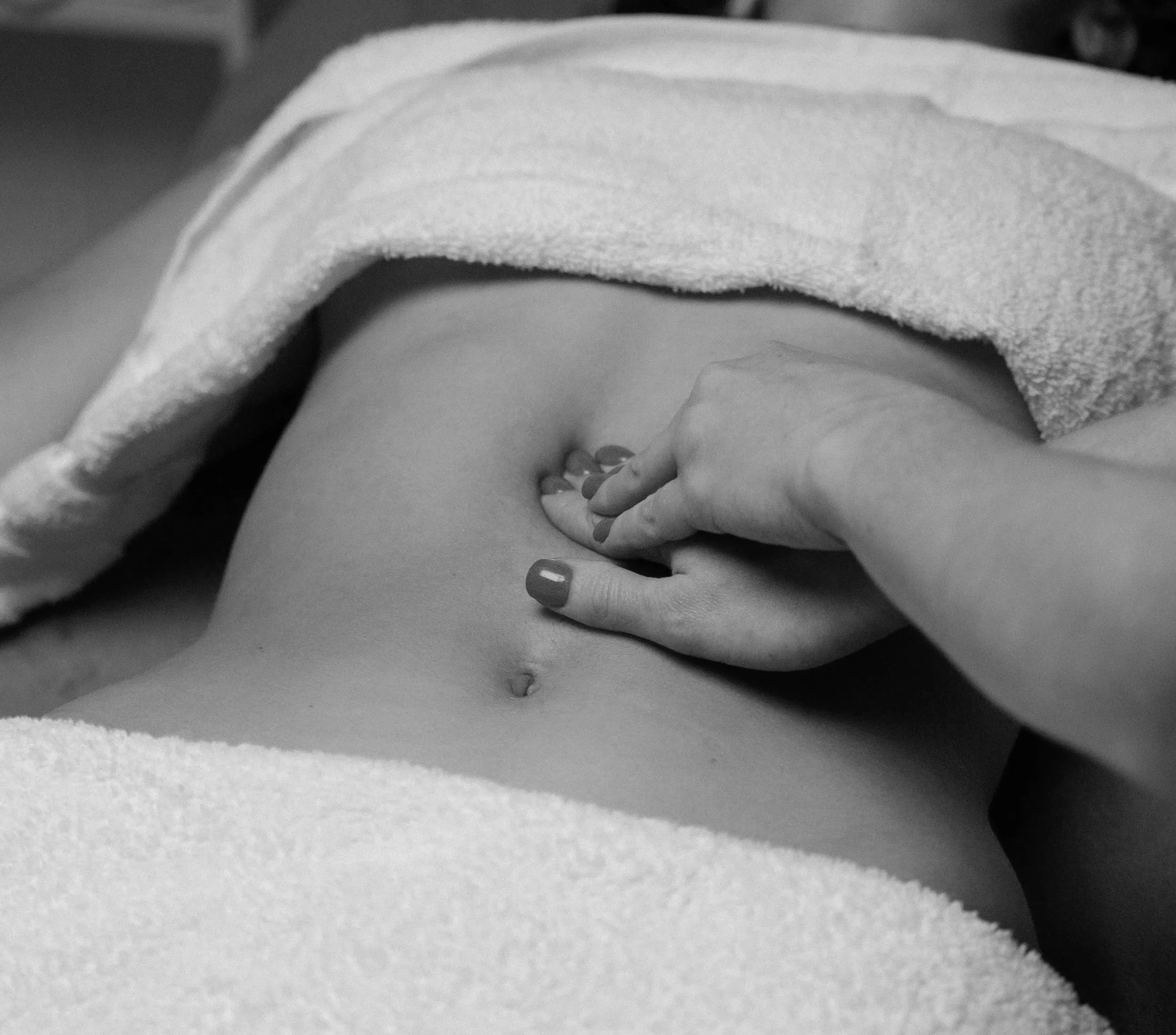 Gros plan d'une main féminine posée sur une surface plane, avec un tissu blanc à proximité et une partie du corps visible en arrière-plan.