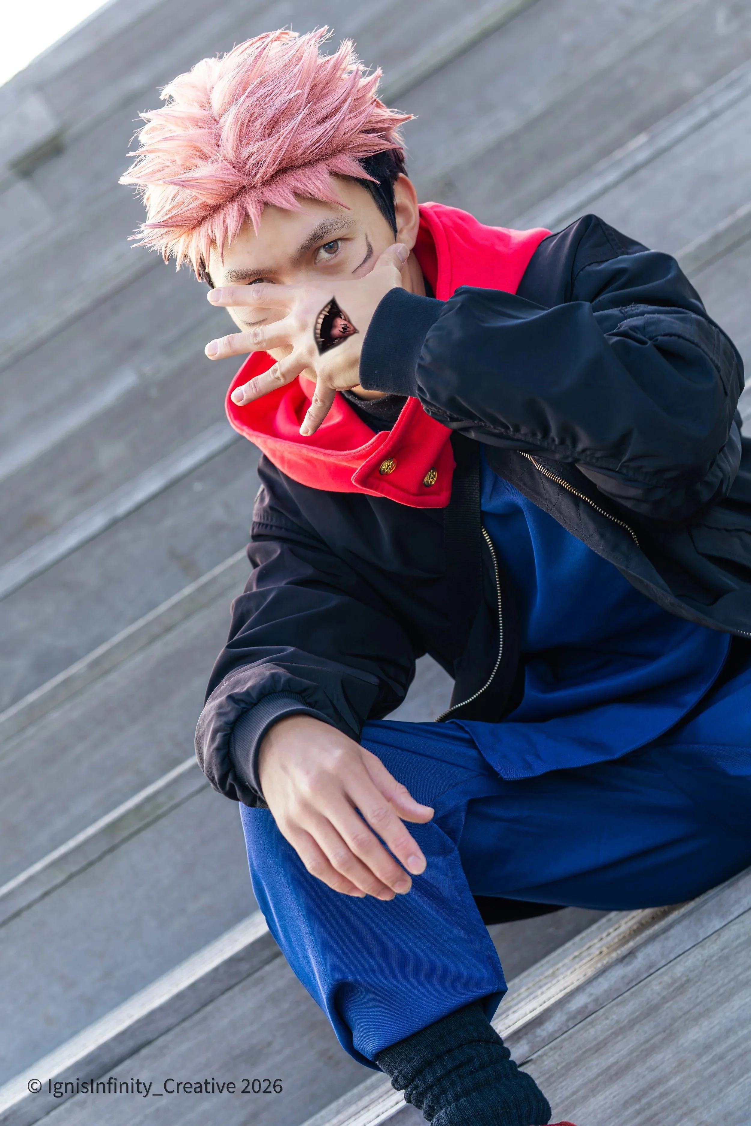 Iconic Yuji Itadori cosplay from Jujutsu Kaisen featuring the terrifying Sukuna mouth hand gesture, captured on urban stairs. Professional shoot by Rotterdam-based cosplay photographer IgnisInfinity Creative.

