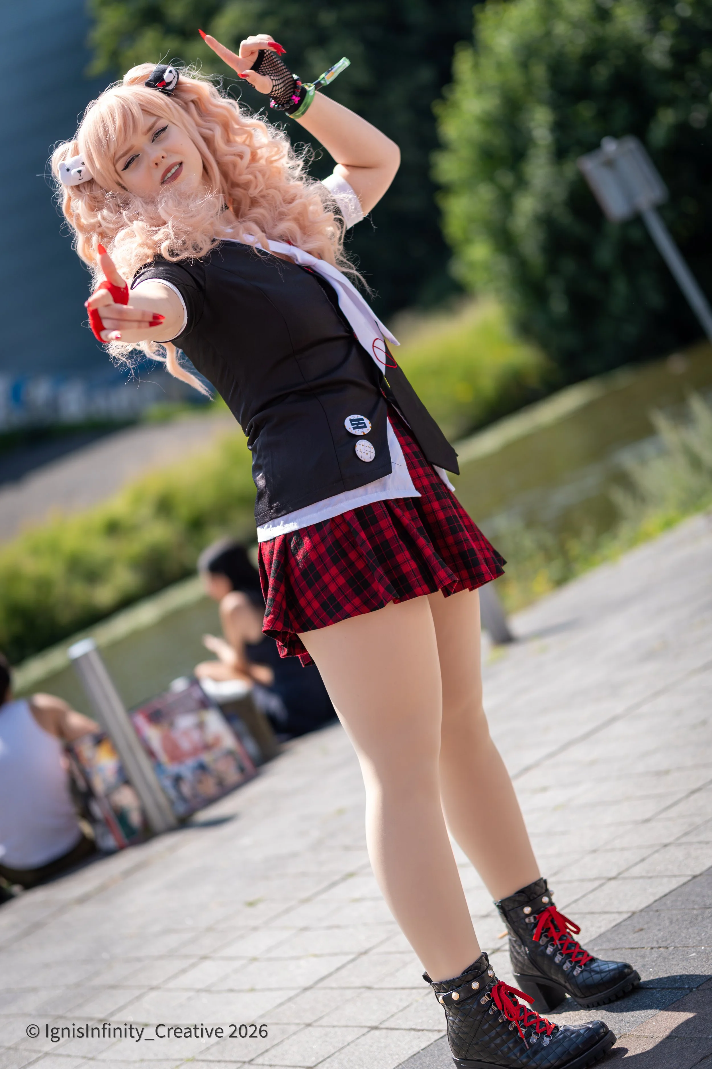 Junko Enoshima (Danganronpa) bringing ultimate despair energy – pink twin-tails, Monokuma clips, red plaid skirt in playful outdoor pose.
Photographer: IgnisInfinity Creative | Cosplayer: @jayindisguise.cos

