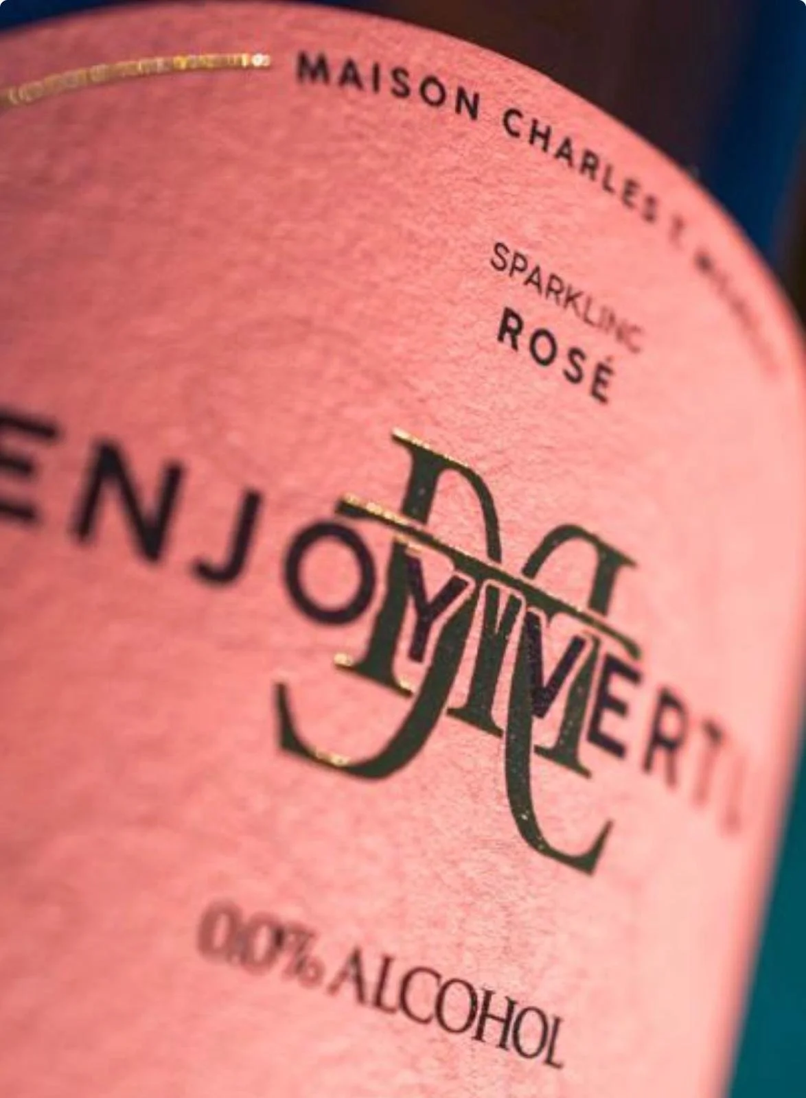 Close-up of a pink sparkling rosé wine label with black and gold text. Title reads 'Enjoyment' with decorative gold accents, and it indicates 12.0% alcohol by volume.