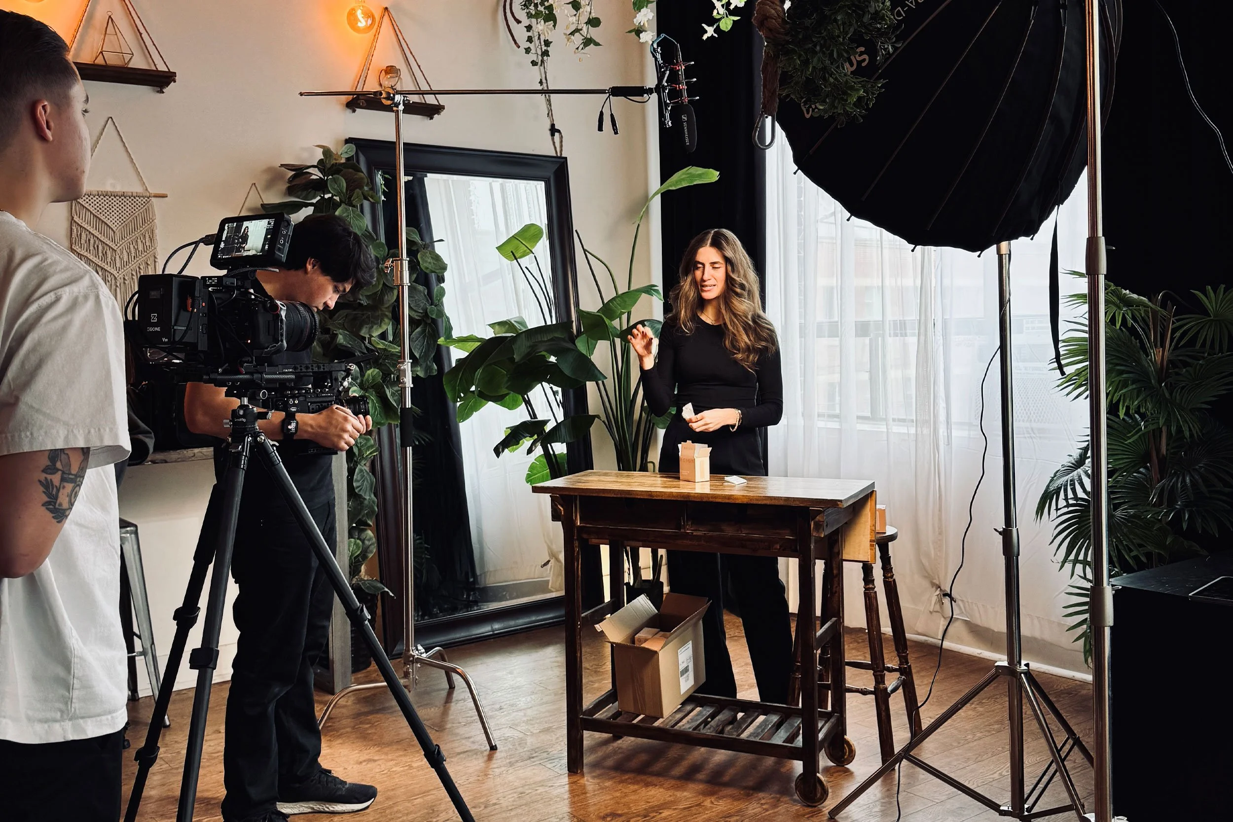 Deadline Creative video production crew filming branded commercial content with professional cameras, studio lighting, and a product presenter in a styled indoor set.