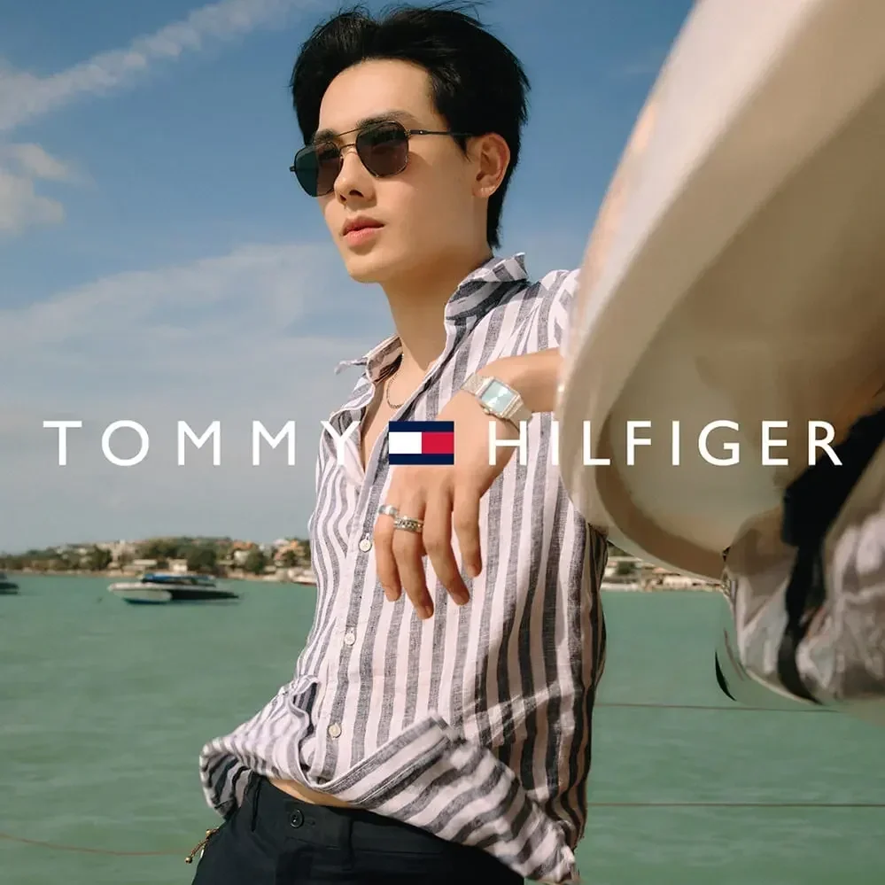 An image of an Asian man wearing low-bridge Tommy Hilfiger sunglasses beside the sea