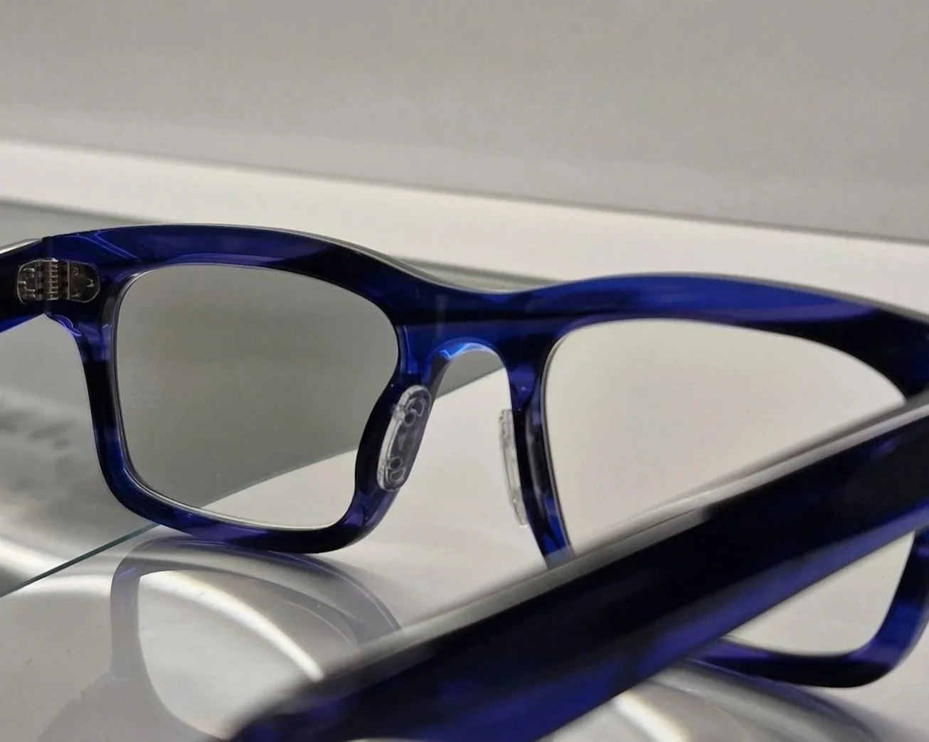 Close-up of a pair of blue eyeglasses resting on a white surface with a gray background