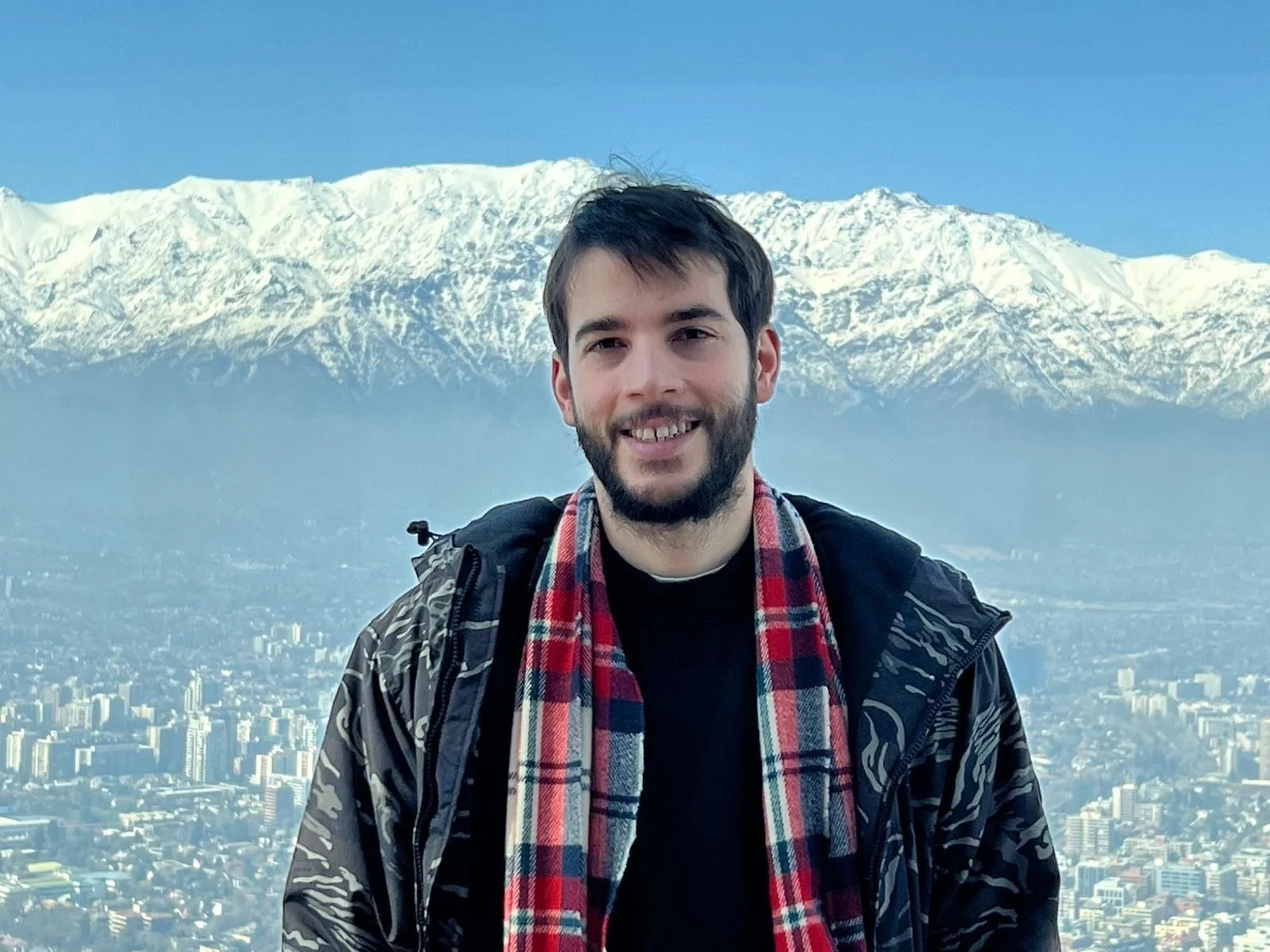 sideOUTsticks CCO, Andrés Scheck,  smiling outdoors in front of a cityscape with snow-capped mountains in the background.