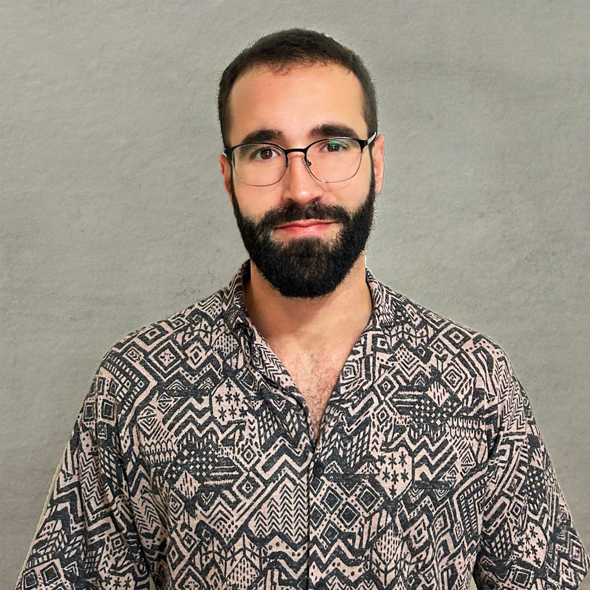 sideOUTsticks Head of AI Audio, Luca Raimondo, with glasses and a beard wearing a patterned shirt, standing against a plain gray wall.