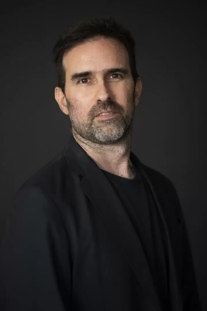 sideOUTsticks CCO, Andrés Scheck,  smiling outdoors in front of a cityscape with snow-capped mountains in the background.