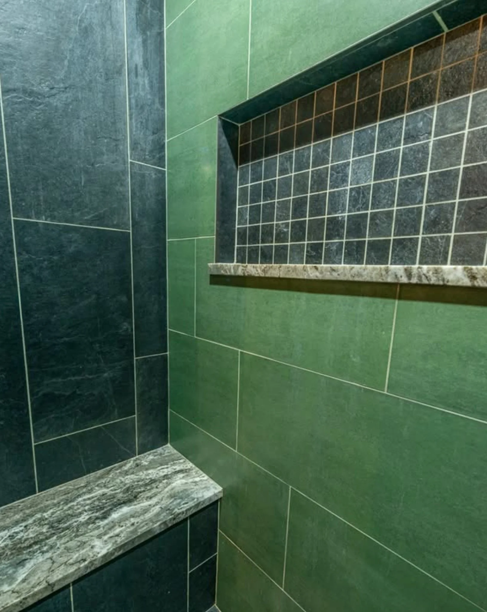 A corner of a bathroom with green and black tiled walls and a marble countertop.