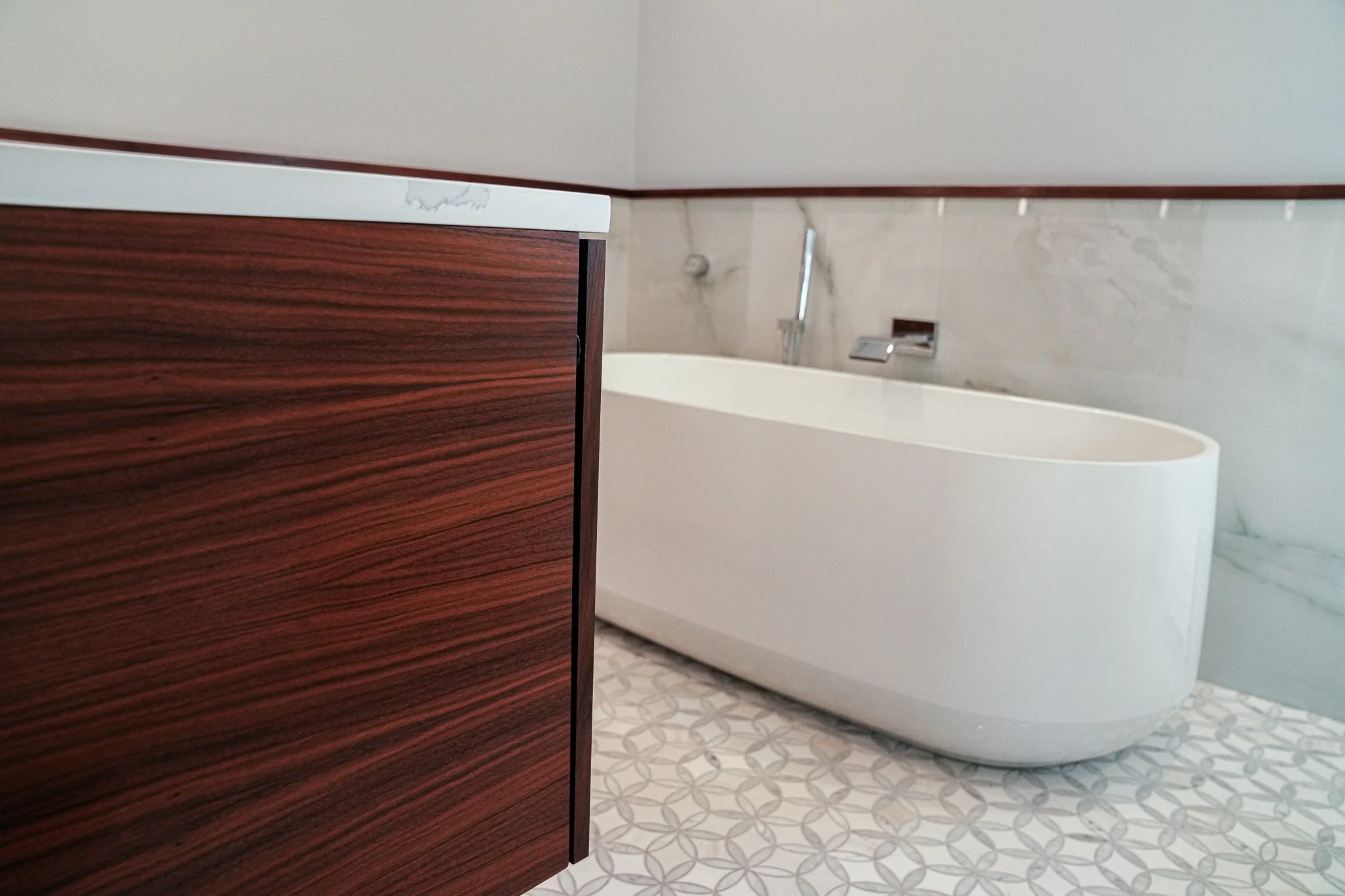A bathroom with a wooden cabinet, a bathtub, a faucet, and patterned floor tiles.