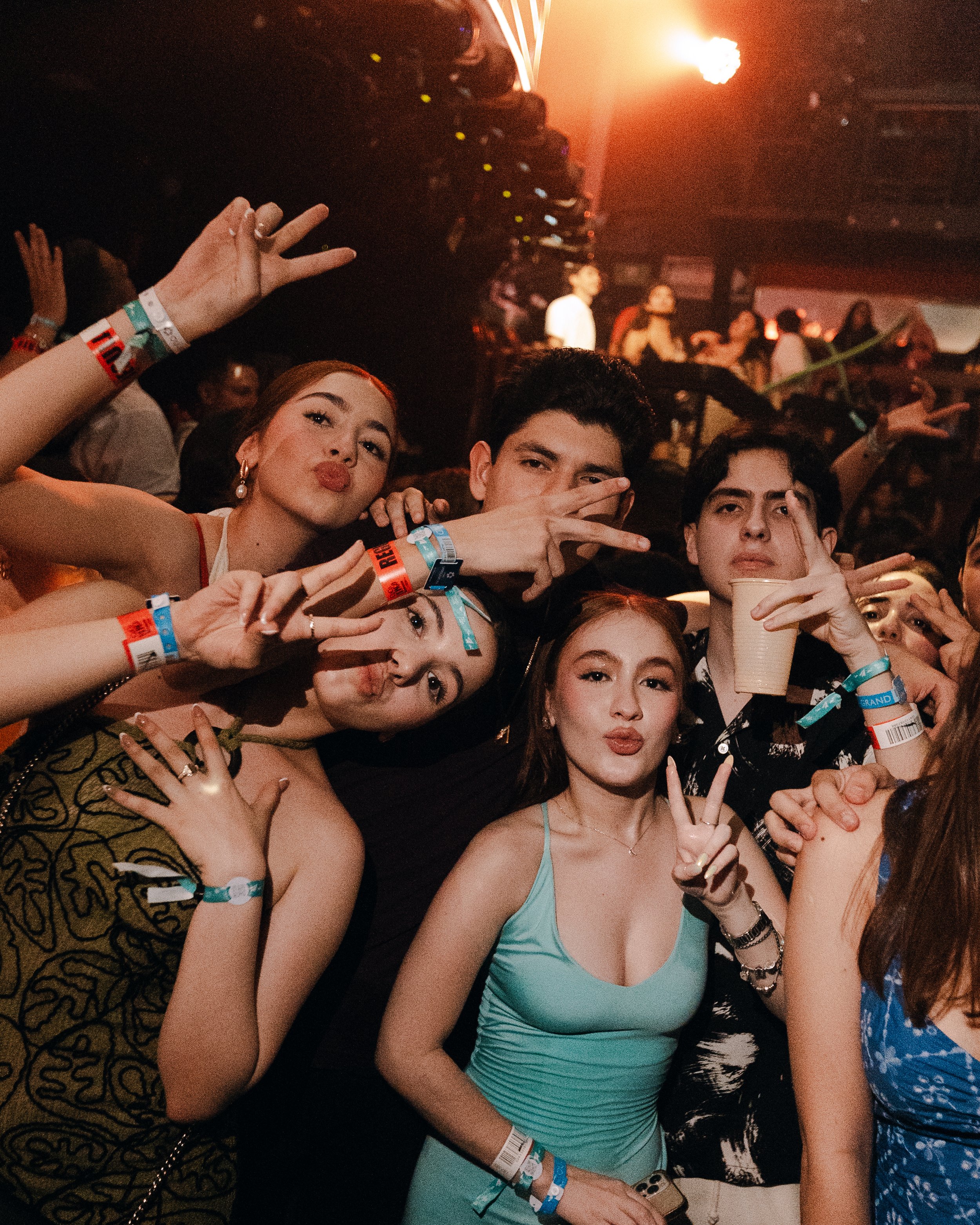 Group of young people at a party taking a selfie, making peace signs and posing.