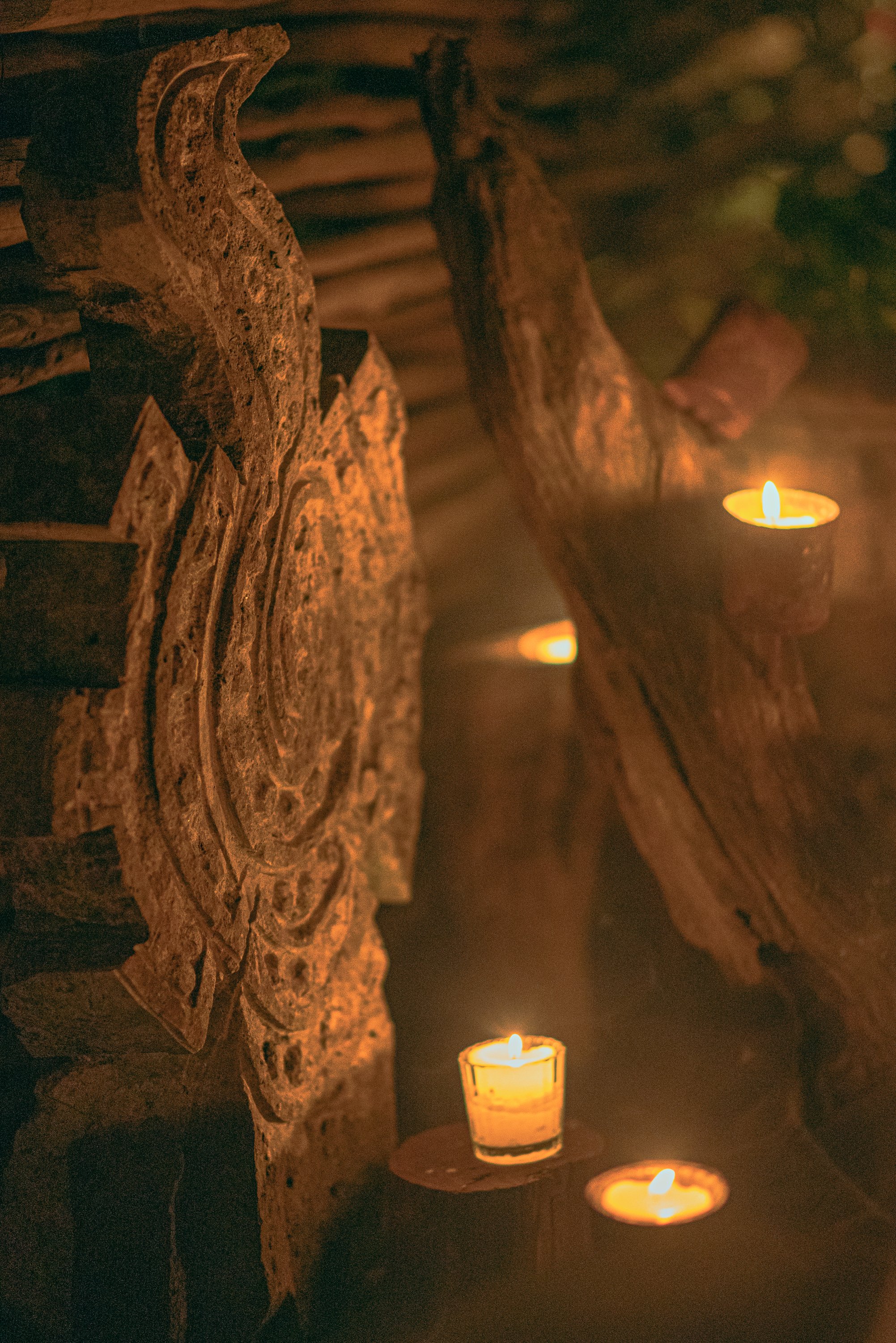Close-up of several lit candles on wooden surfaces with a rustic, logs and textured bark background, creating a warm and cozy ambiance.