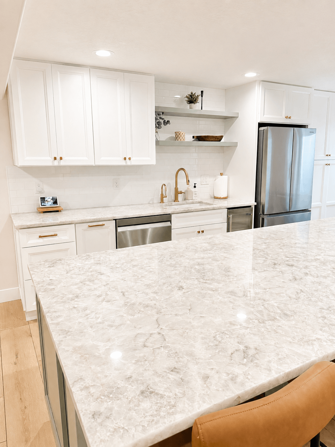 Modern kitchen with white cabinets, marble countertops, stainless steel appliances, and open shelving.