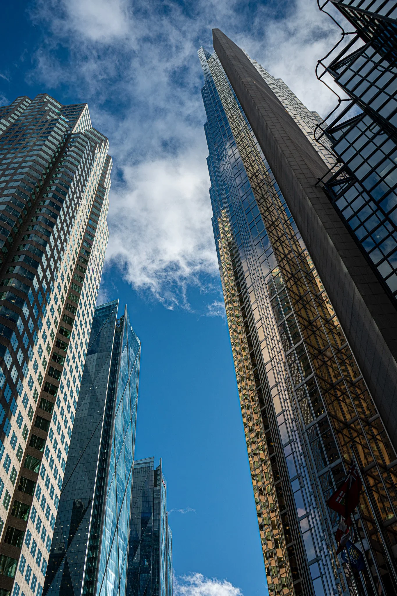 Upward architectural view of layered glass towers, reflective surfaces capturing moving clouds and shifting light across vertical lines.