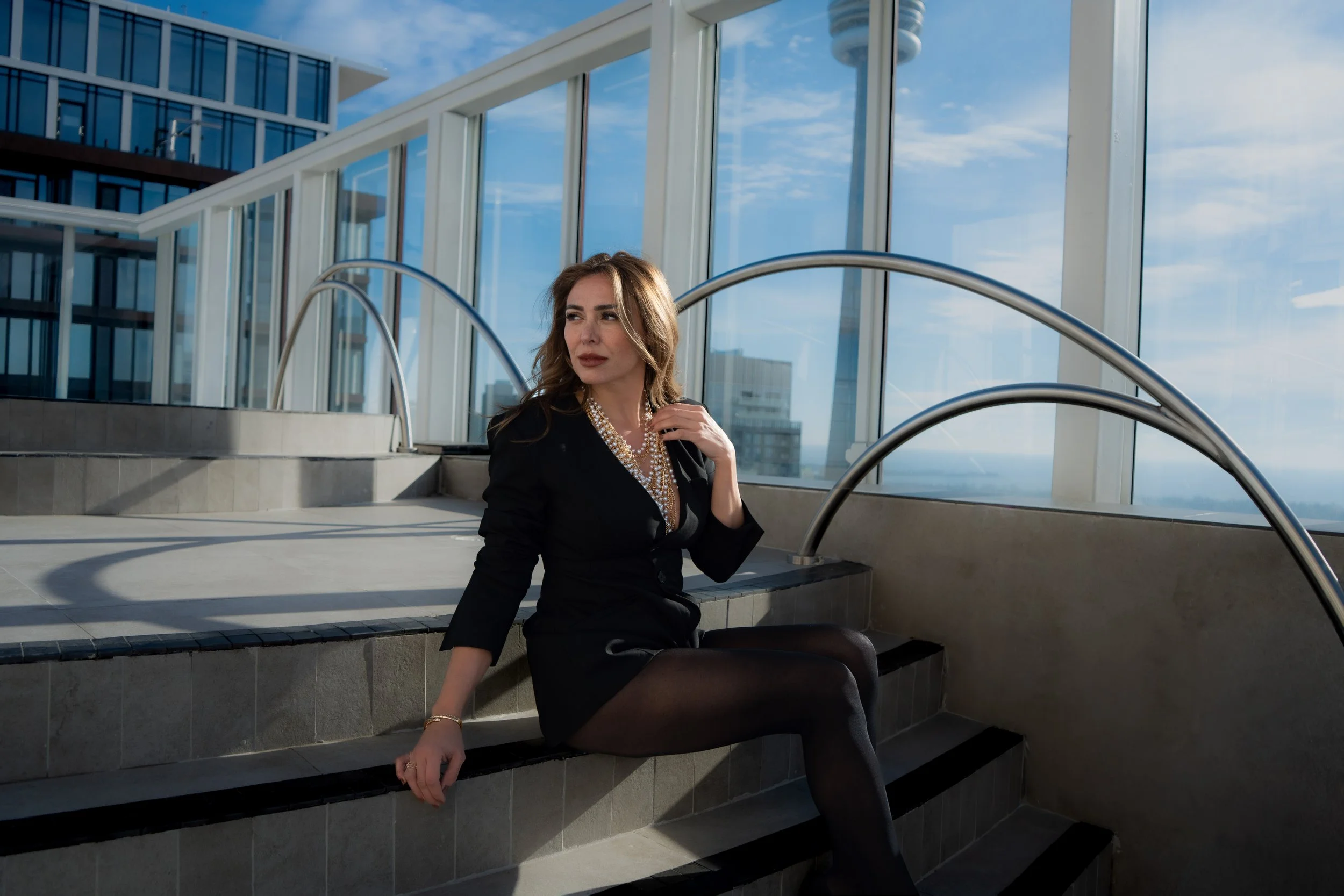 Fashion portrait on an urban terrace with curved railings and city skyline, tailored black outfit styled with natural light and clean composition