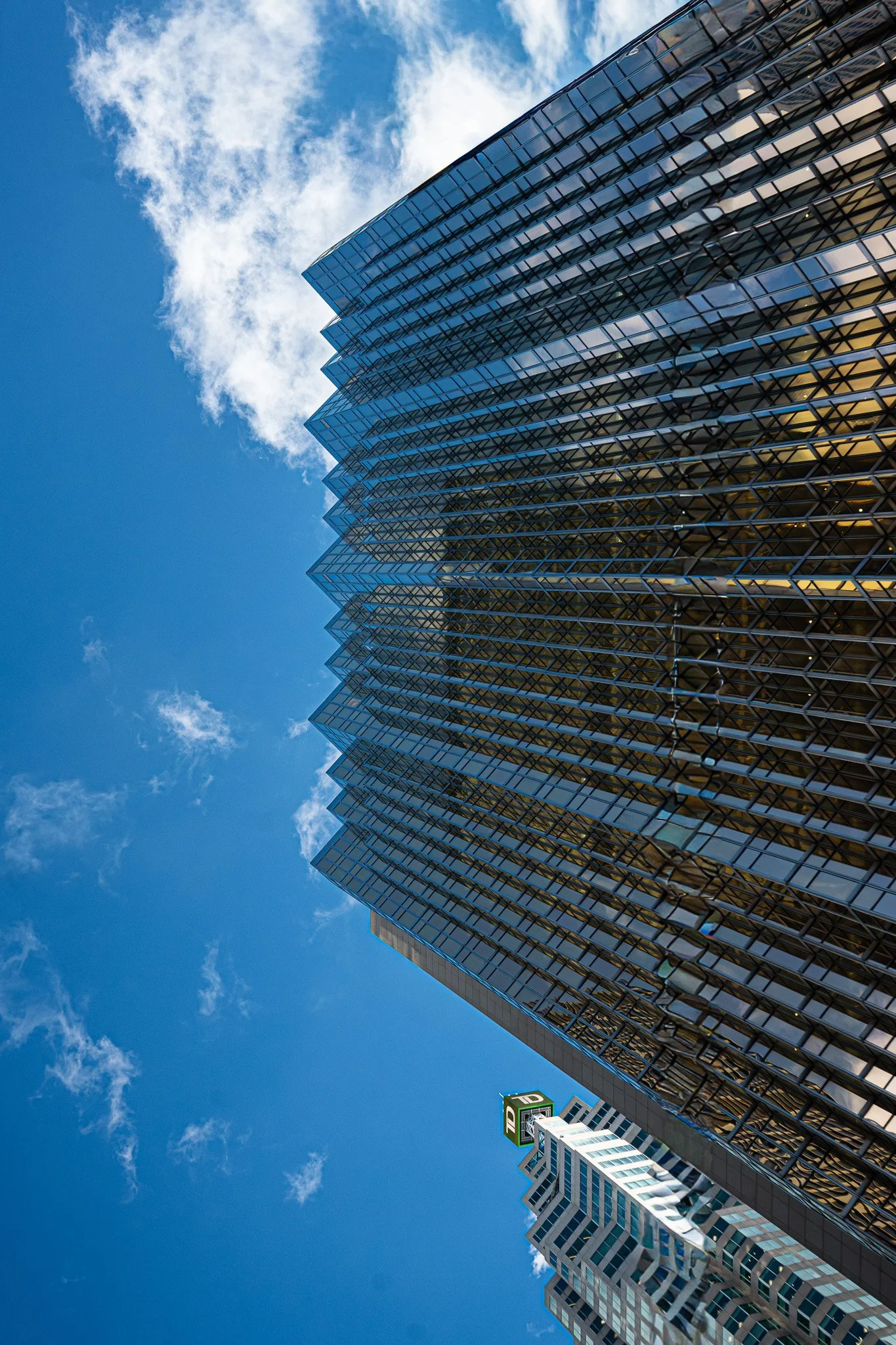 Curved glass high-rise against open sky, façade reflecting surrounding city and light to create a sense of motion and fluidity.
