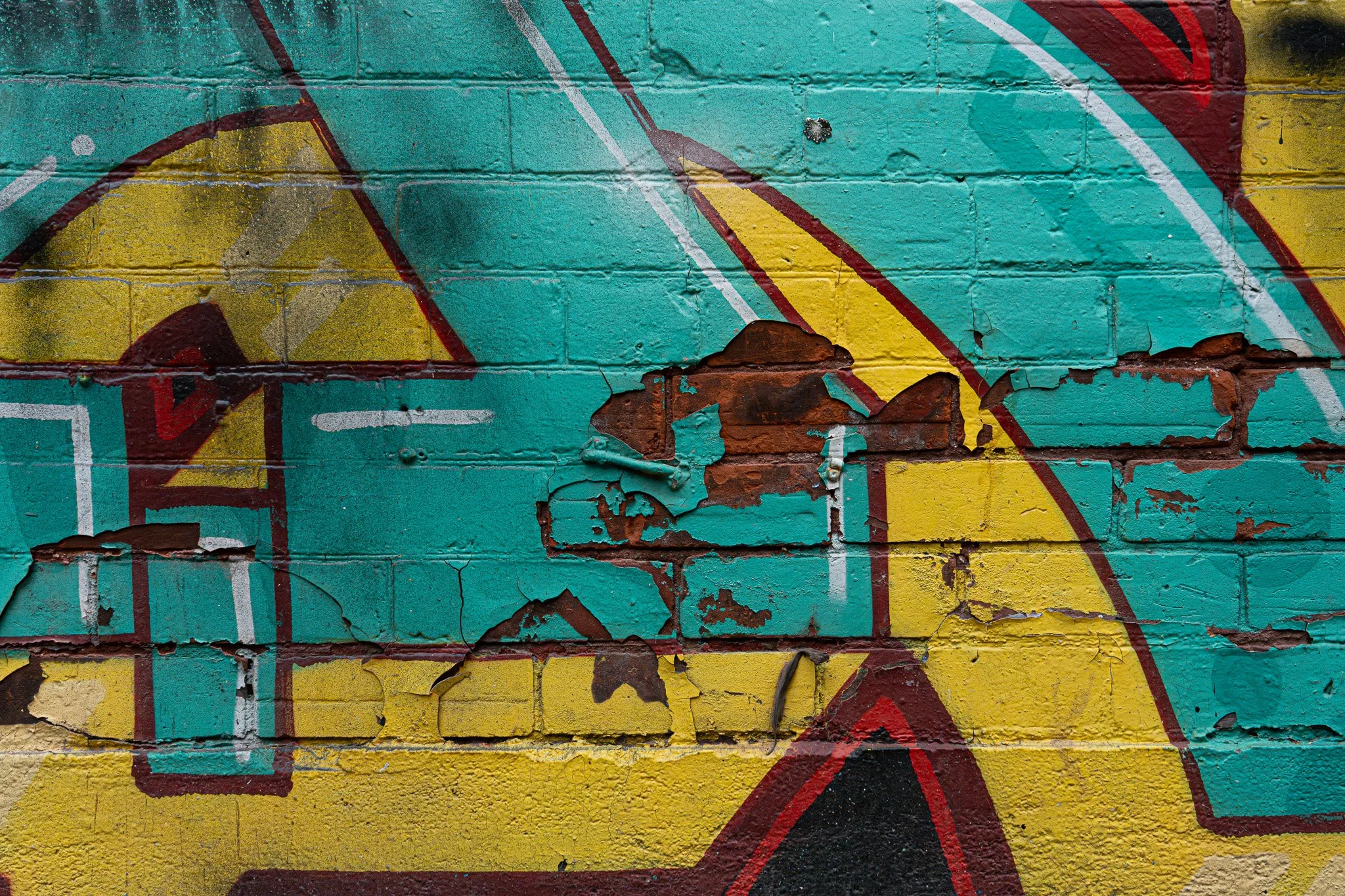 Close-up of layered graffiti on a brick wall, peeling paint revealing texture, age, and urban color contrast.