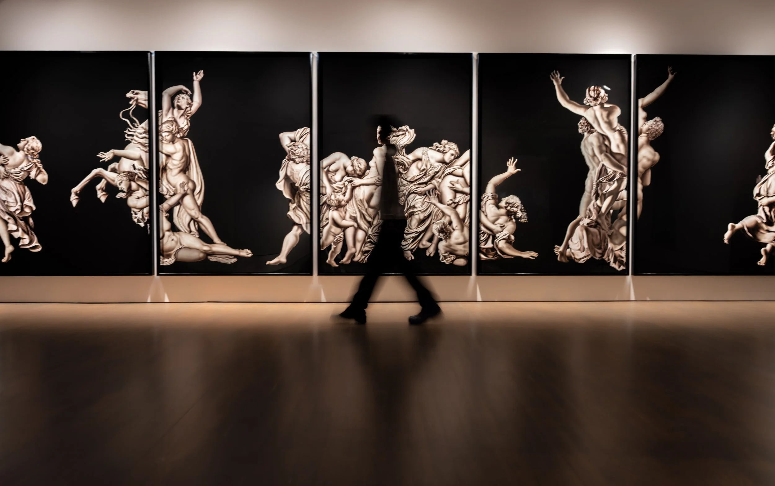 Large-scale paintings displayed across a gallery wall, featuring classical figures in high contrast. A blurred human figure walks through the frame, reinforcing the concept of movement within still imagery. Part of the “We Move Through” visual series