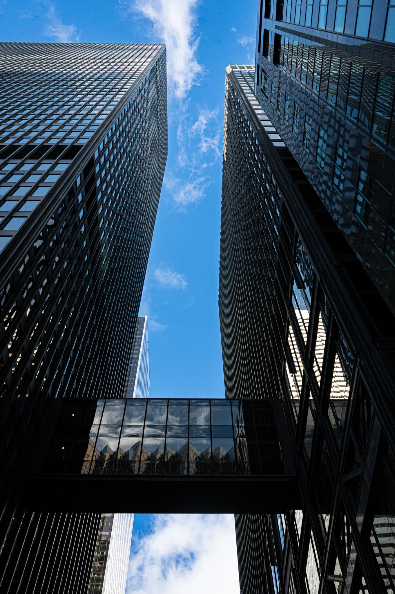 Framed perspective between dark buildings revealing a strip of blue sky, highlighting contrast, depth, and reflective geometry.