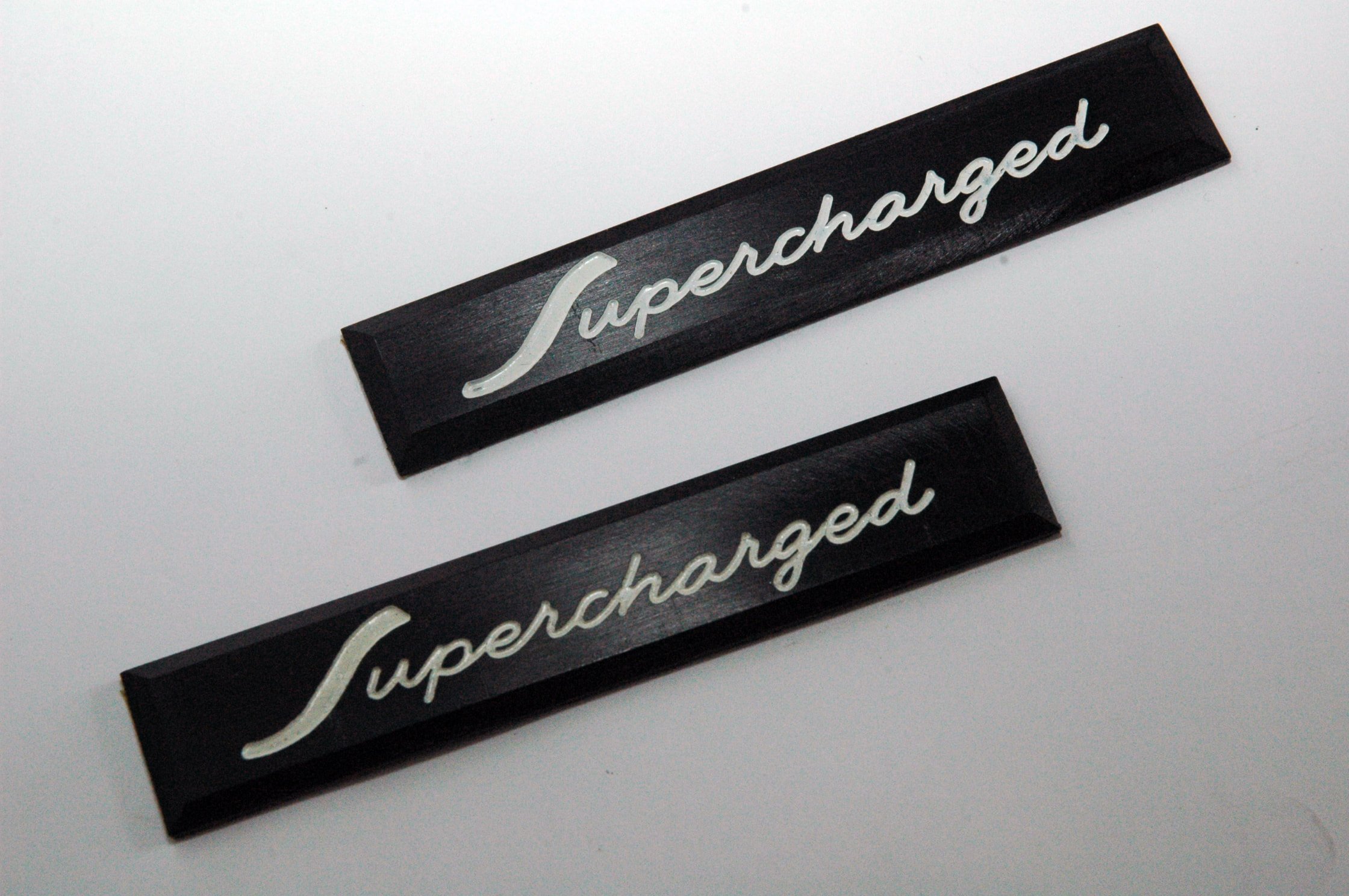 Pair of black anodized aluminum Supercharged emblems with white etched lettering for Studebaker Avanti R2 and R3 restoration.