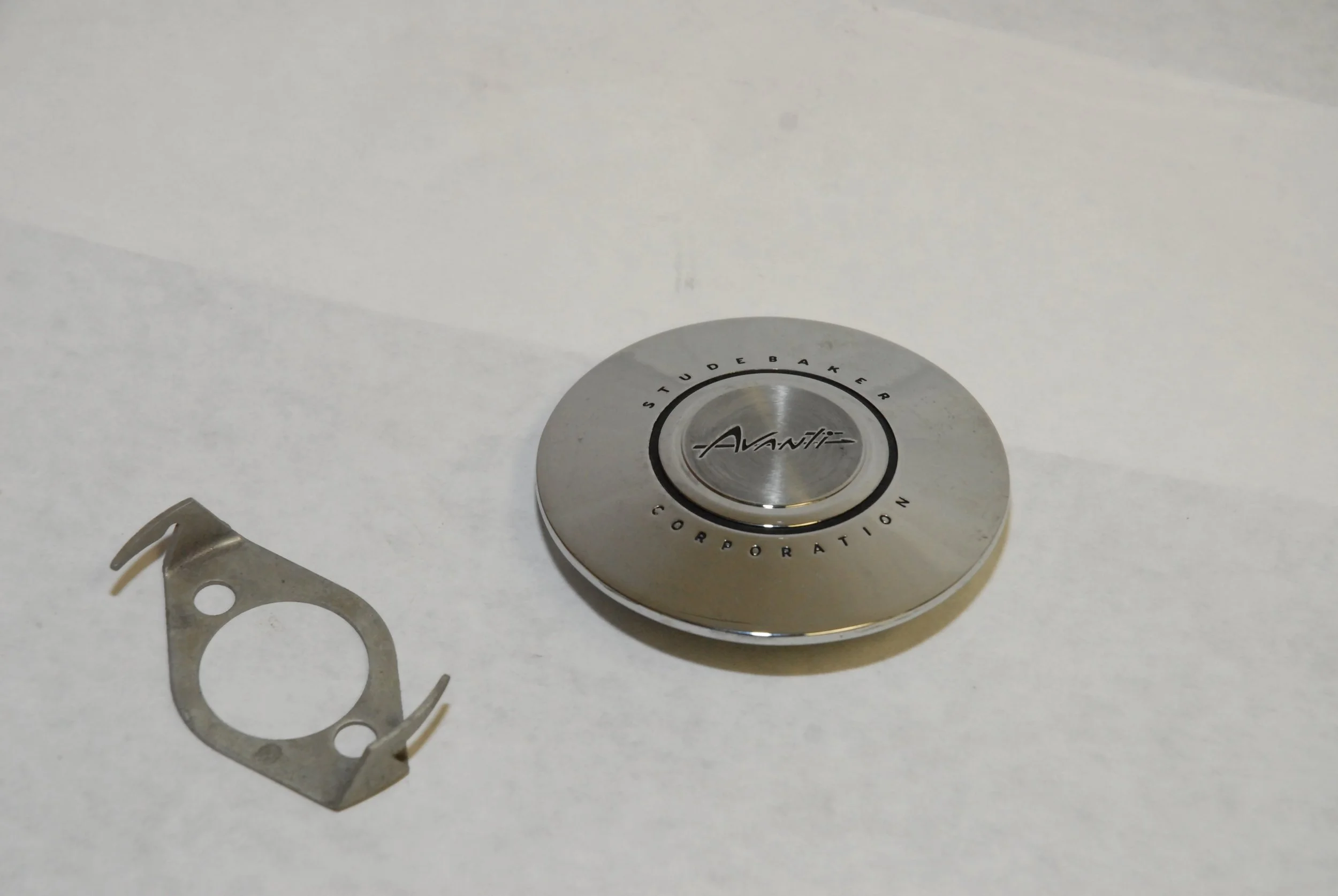 NOS Chrome Steering Wheel Center Cap Emblem and Retainer Clip for 1963-1971 Studebaker Avanti, Parts 1557383 and 1557894.