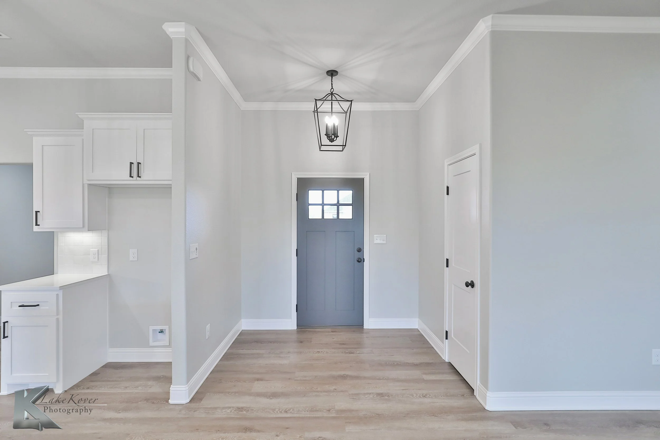 Empty entryway with a gray front door, a black metal lantern-style ceiling light, white walls, light wood flooring, and two white doors.