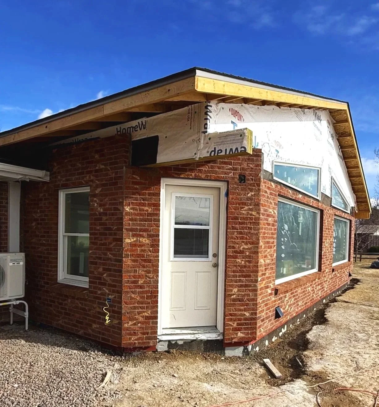 A house under construction with brick exterior, unfinished roof, and construction materials visible.