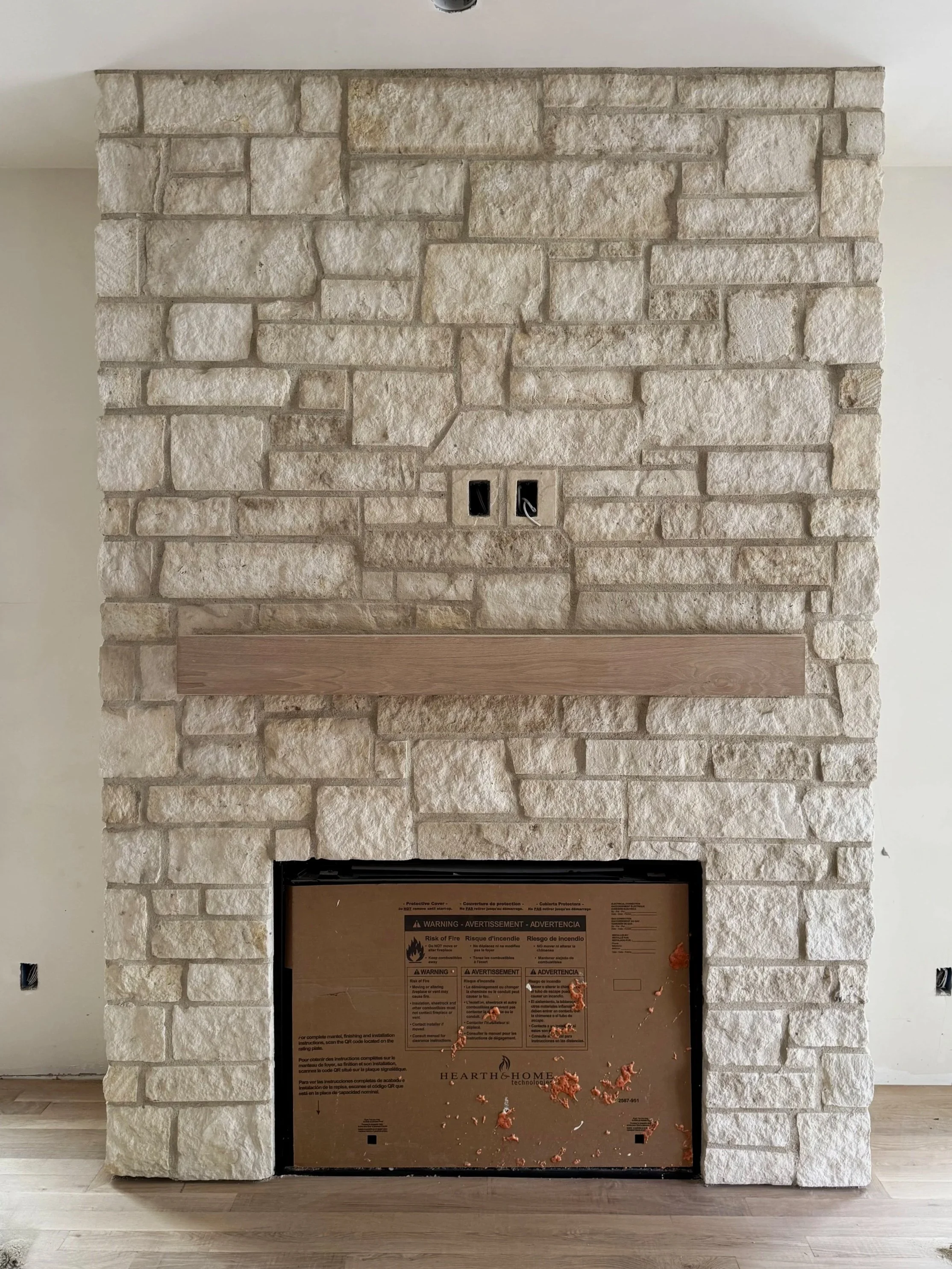 Stone fireplace with a wooden mantel and an opening for a firebox, surrounded by cream-colored bricks in an indoor setting.