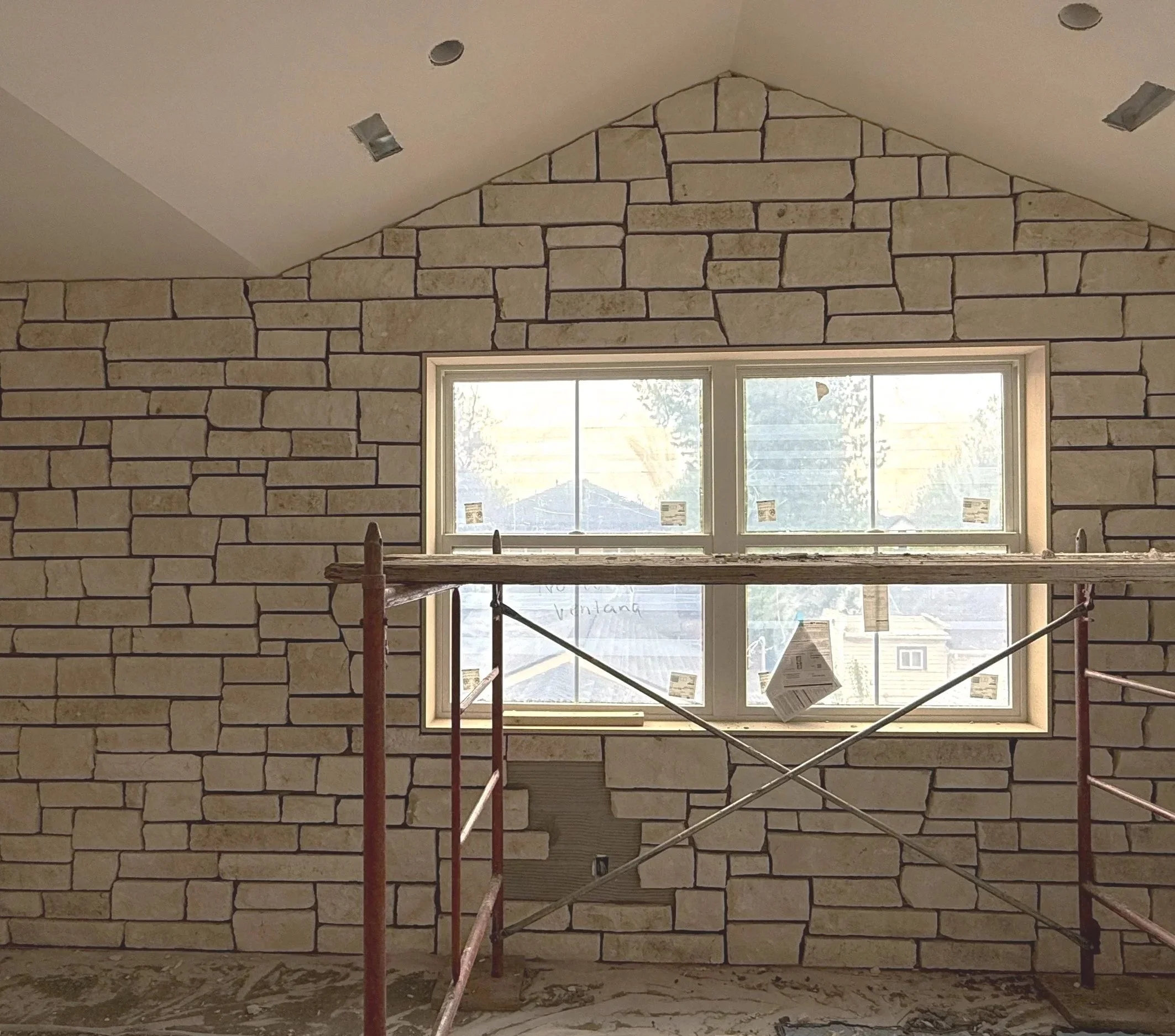 Interior wall under construction with a stone veneer and a window, scaffolding in the foreground.