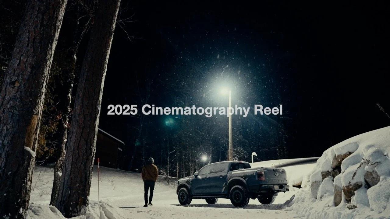 A snowy nighttime scene with a person walking near a parked pickup truck, illuminated by streetlights, in a wooded area.