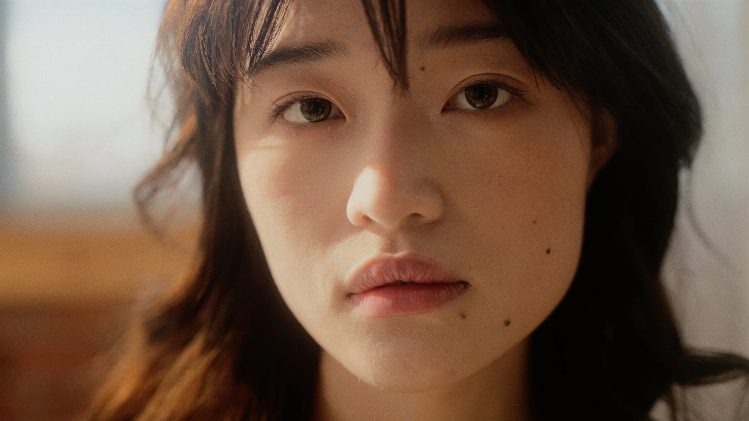 Close-up of a woman's face with light skin, dark brown hair, and brown eyes, looking directly at the camera.