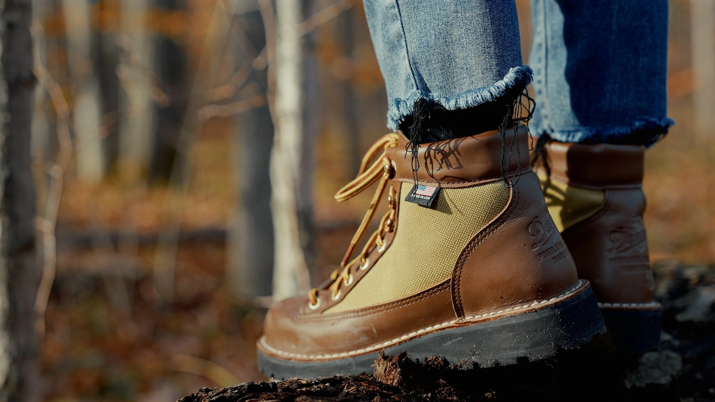Close-up of person wearing tan and brown hiking boots and ripped jeans in a forest.