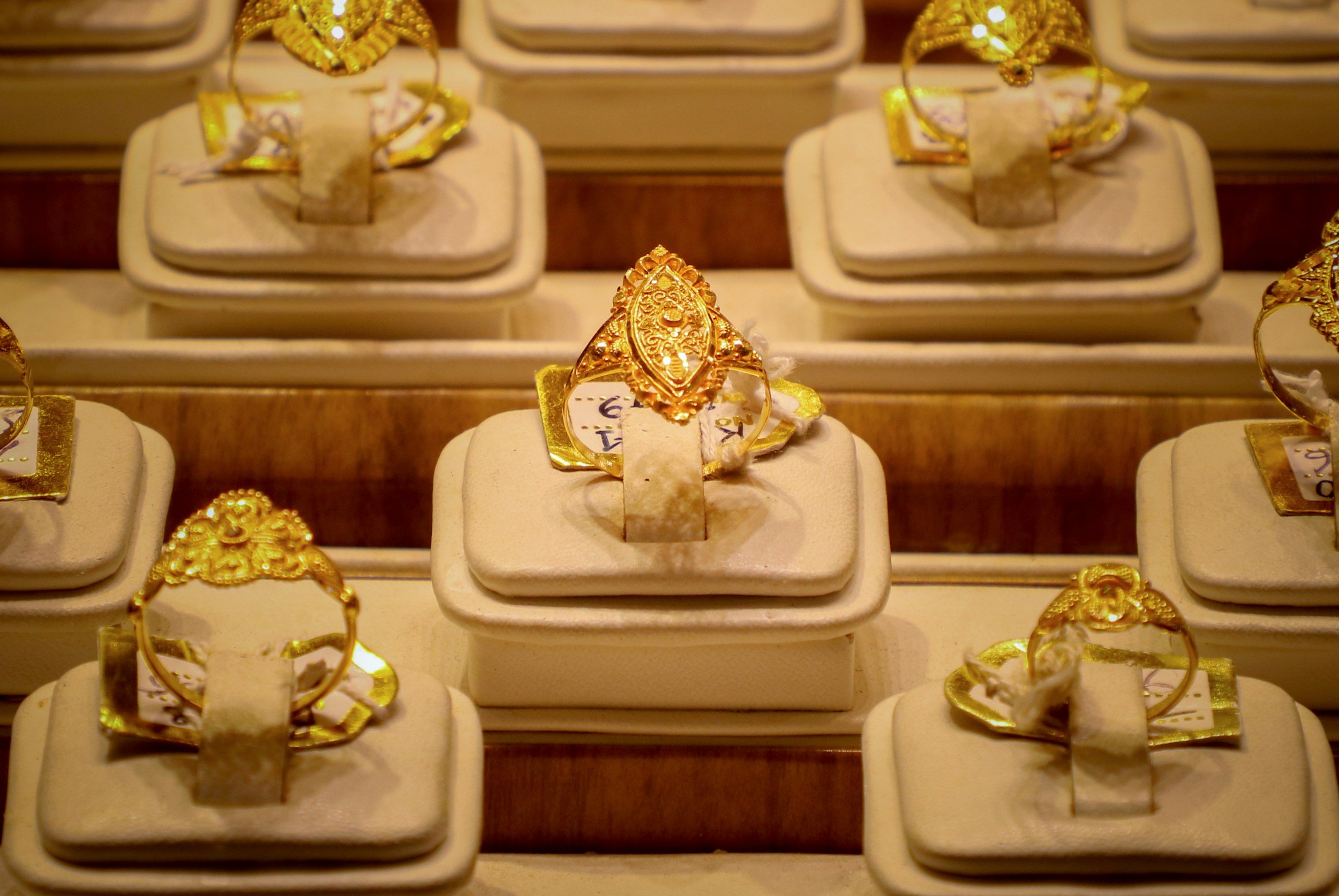 Gold rings displayed on beige jewelry stands in a jewelry store display case.