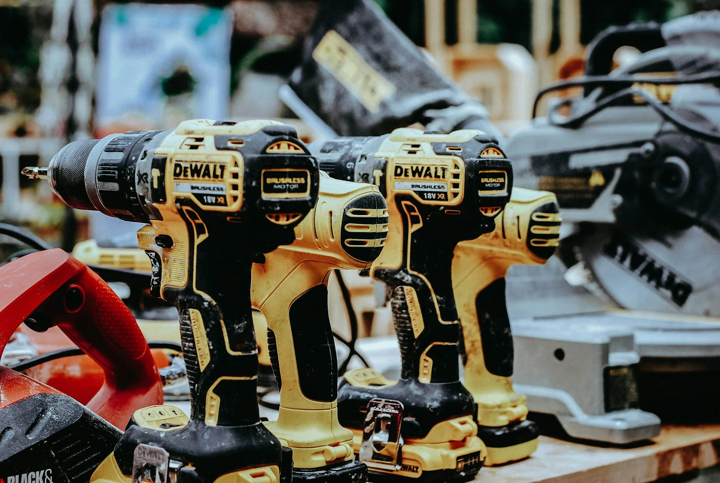 Several yellow DeWalt cordless power drills lined up on a workbench in a workshop.