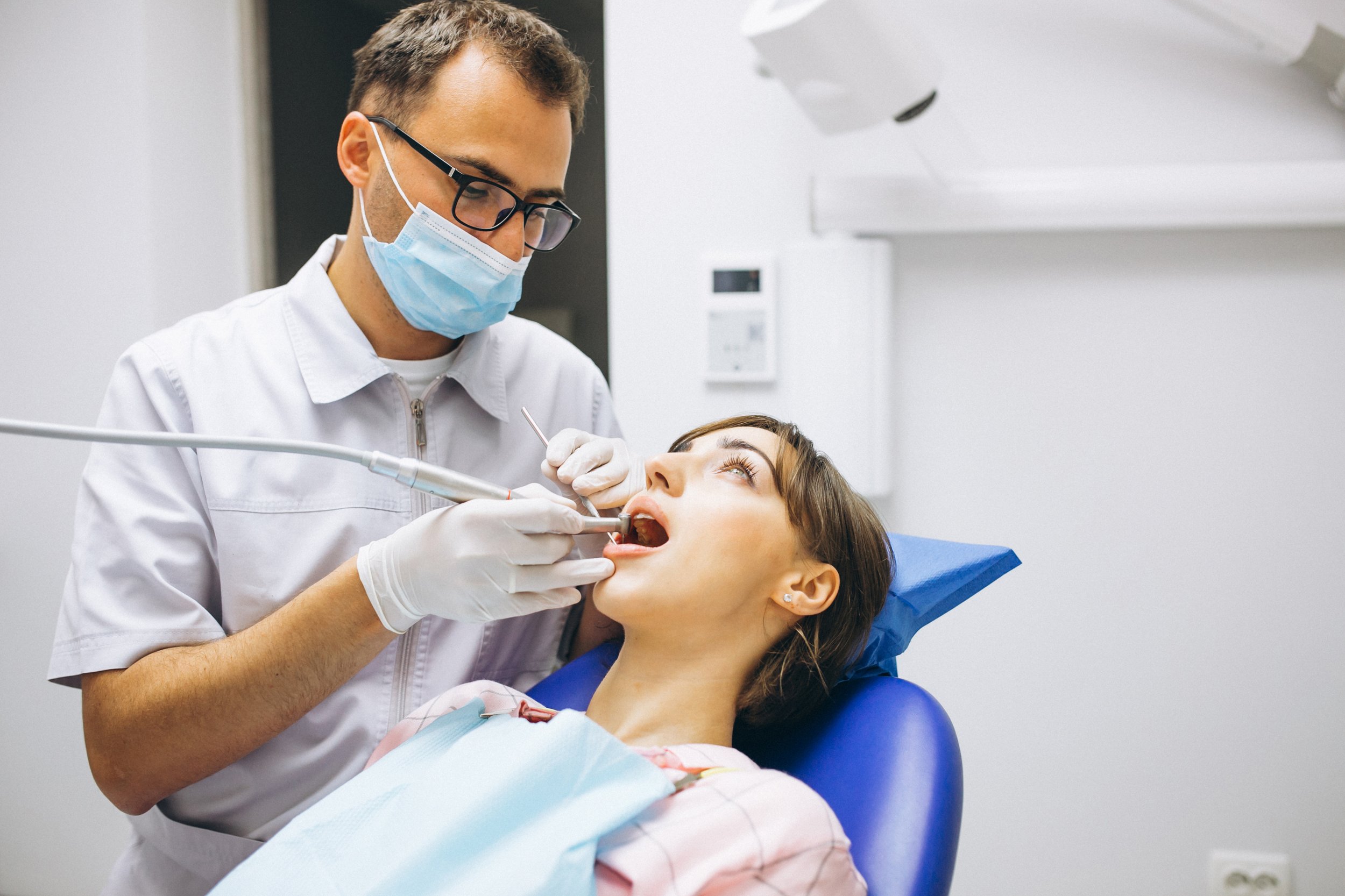 Dentista atendiendo a una mujer en una clínica, usando mascarilla y guantes, realizando un procedimiento dental.