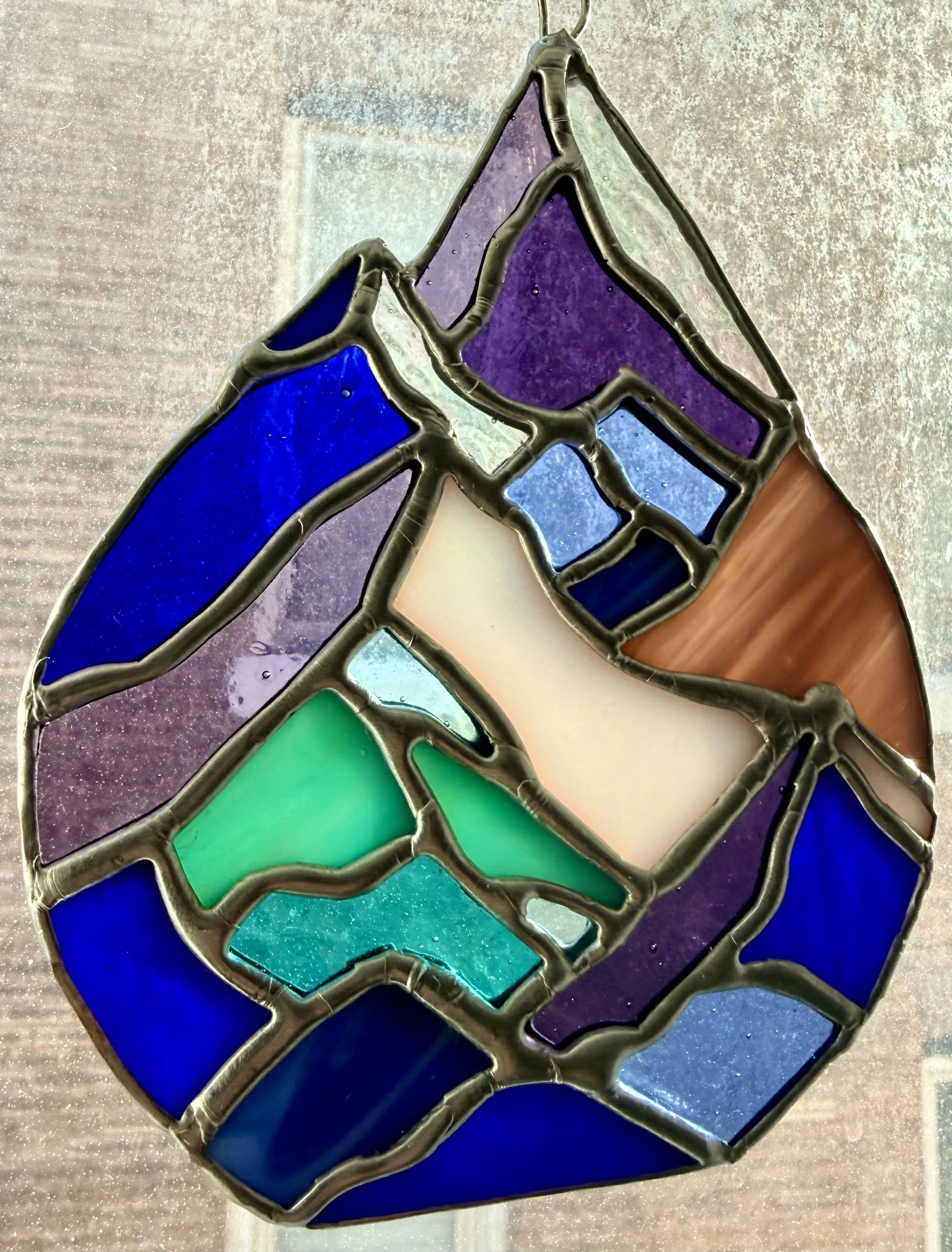 Colorful stained glass mountain range with abstract geometric patterns in purple, blue, green, white, pink, and clear glass.