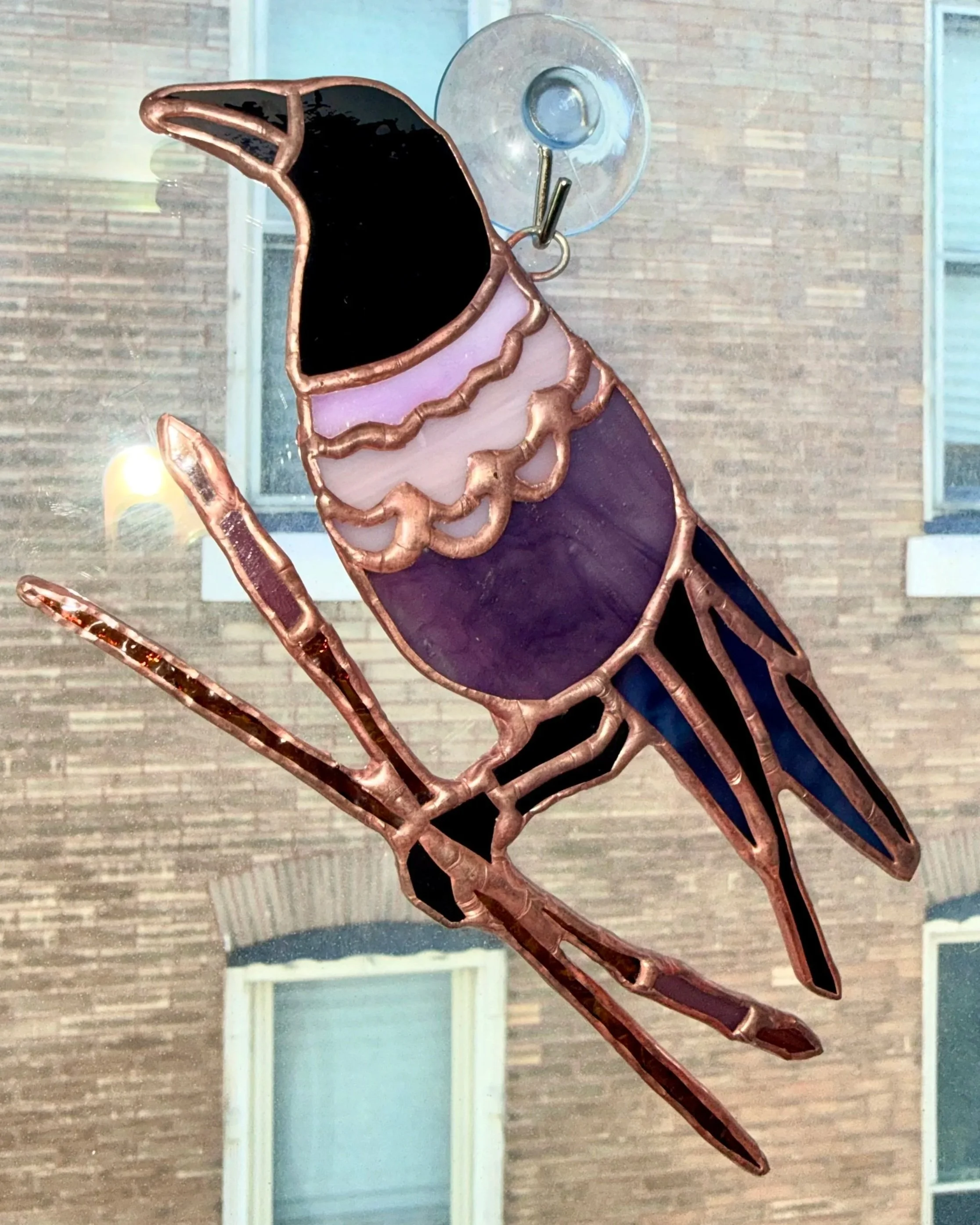 Stained glass window depicting a colorful bird sitting on a branch, with a background of window and building.