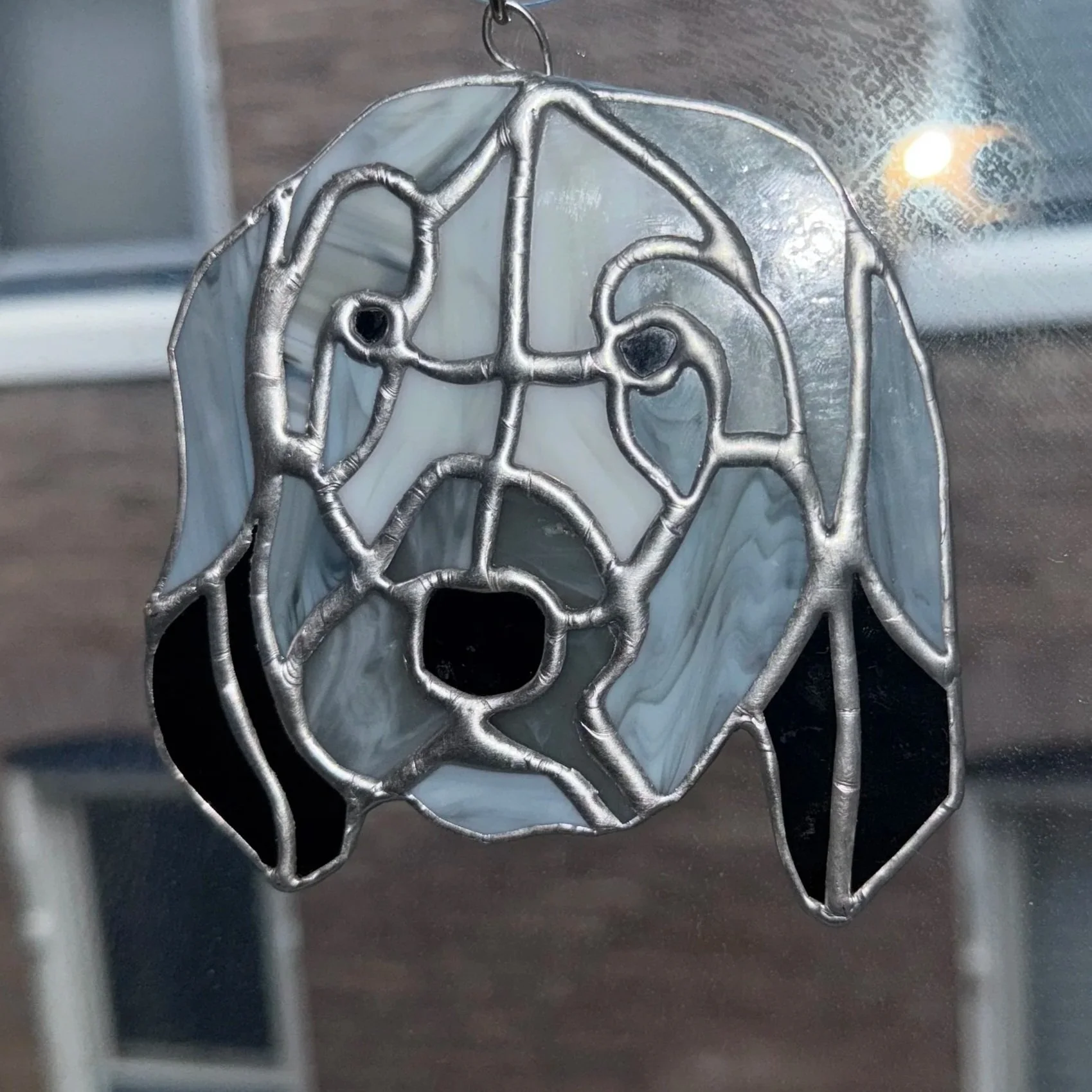 Decorative stained glass stained glass hanging of a dog, with black, gray, and white colors, framed with silver metal.
