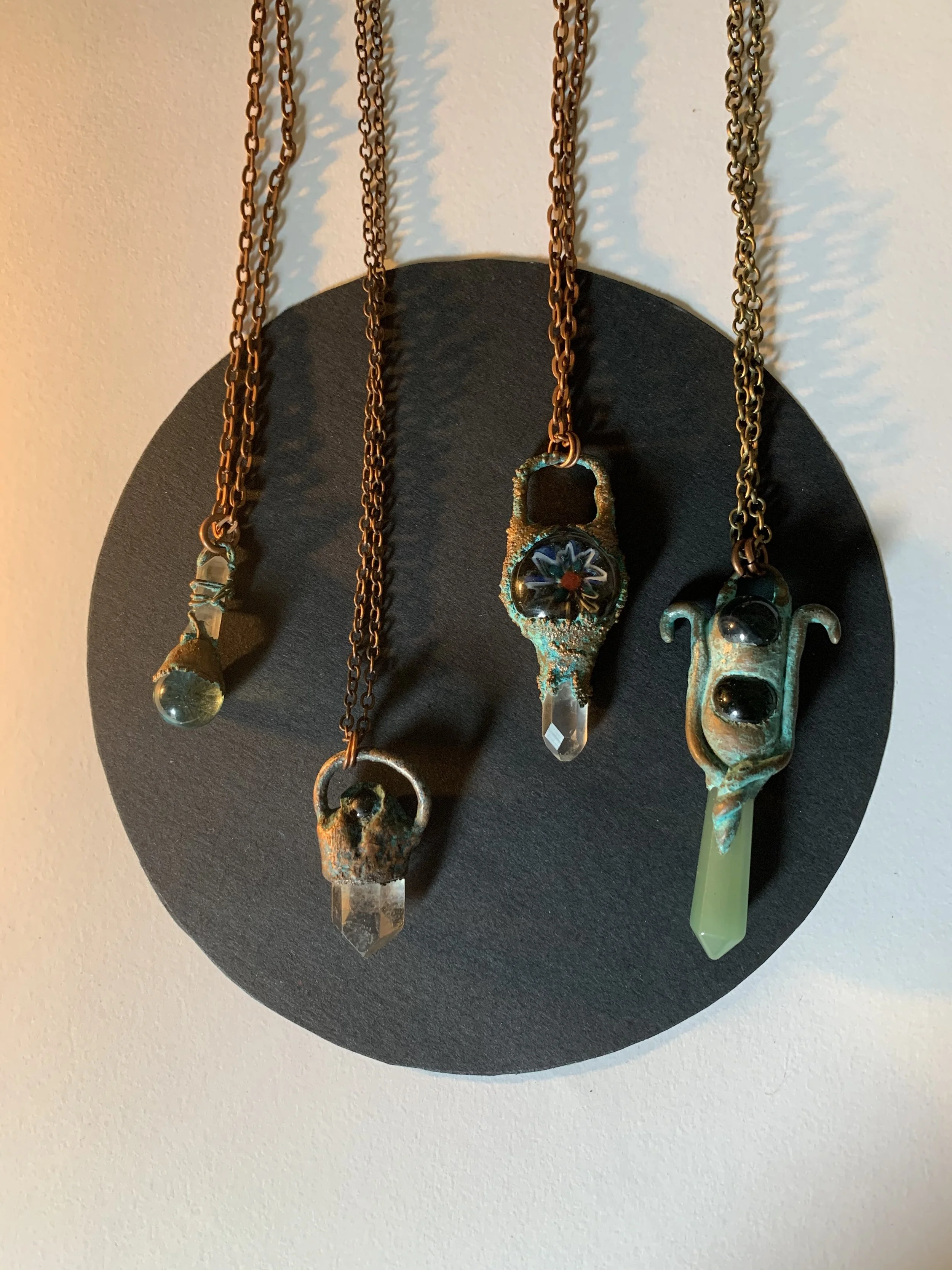 Four necklaces with pendants hanging on a black circular display against a light background.