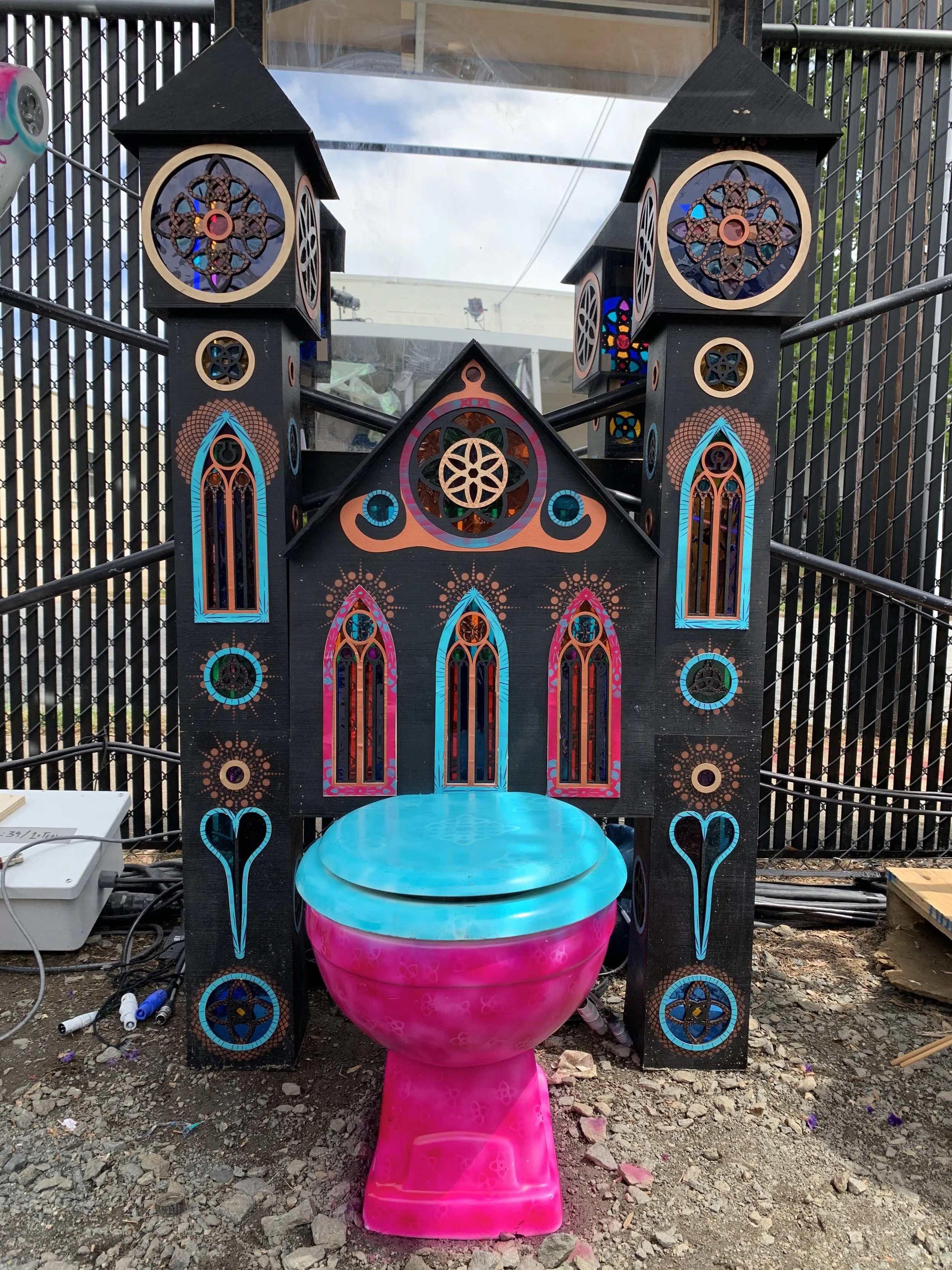 Decorative, colorful throne or seat designed to look like a church, with neon pink and blue accents, surrounded by Gothic-style architectural elements with intricate patterns and stained glass-like details.