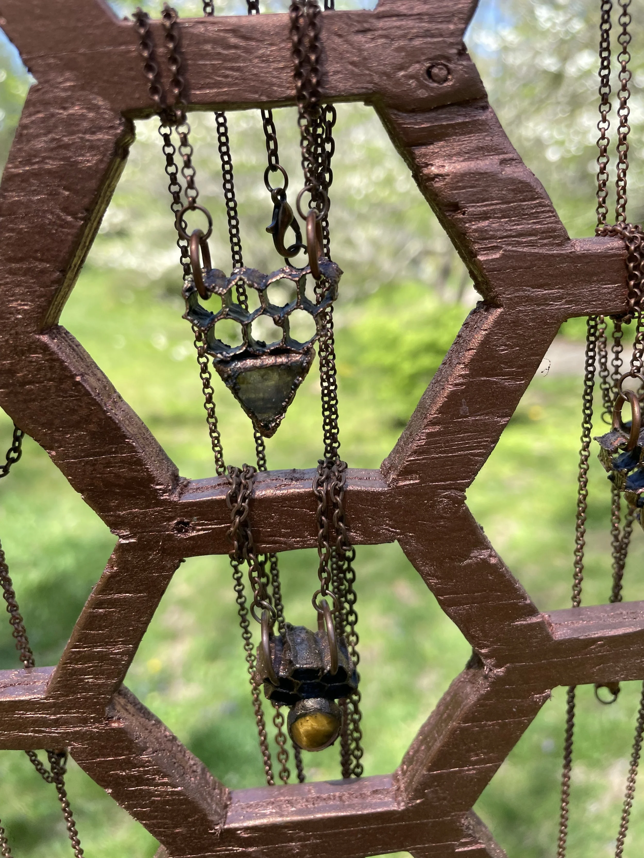 Close-up of vintage jewelry hanging on a wooden star-shaped display, with a blurred green outdoor background.