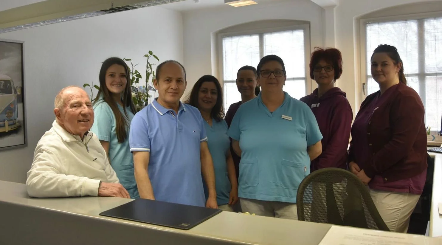 Ein Team von neun Personen, bestehend aus Pflegepersonal und Ärzten, steht in einem Krankenzimmer vor einem Schreibtisch, lächelt und schaut in die Kamera.