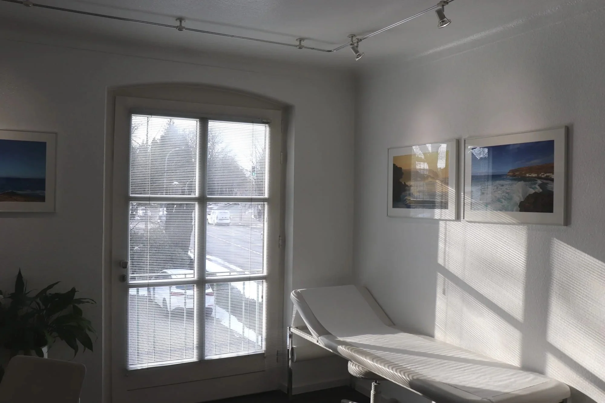 Ein Behandlungsstuhl in einem hellen Raum, mit Fenstern, durch die Sonnenlicht und Schatten fallen, sowie Wandbilder mit Meeresbildern.