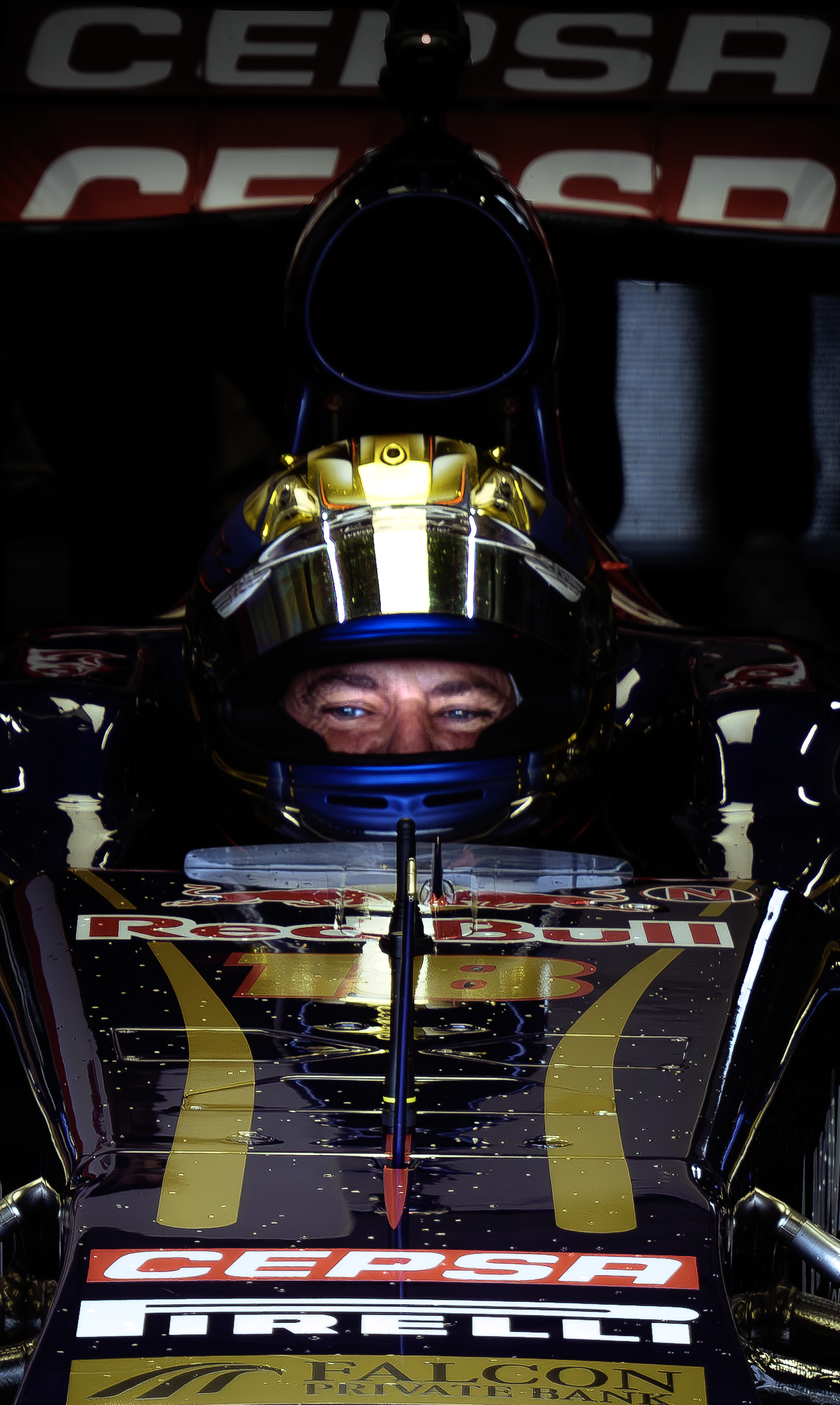 Un pilote de course automobile dans son cockpit, portant un casque doré, assis dans une voiture de course avec des logos de Red Bull, Cepsa, Pirelli et Falcon.