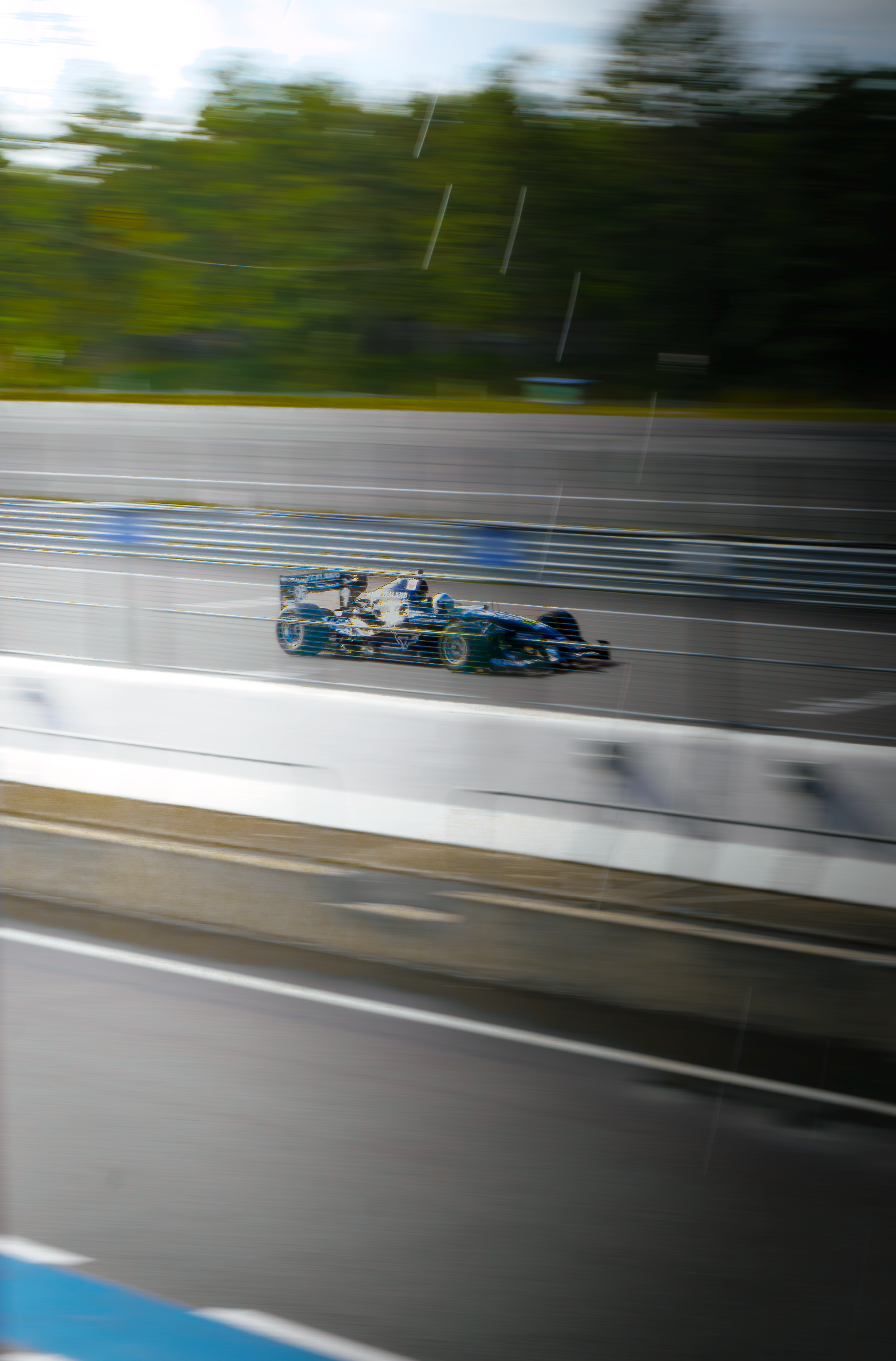 Voiture de course de Formule 1 en mouvement sur un circuit, vue floue en raison de la vitesse, avec un focus sur la voiture au centre.