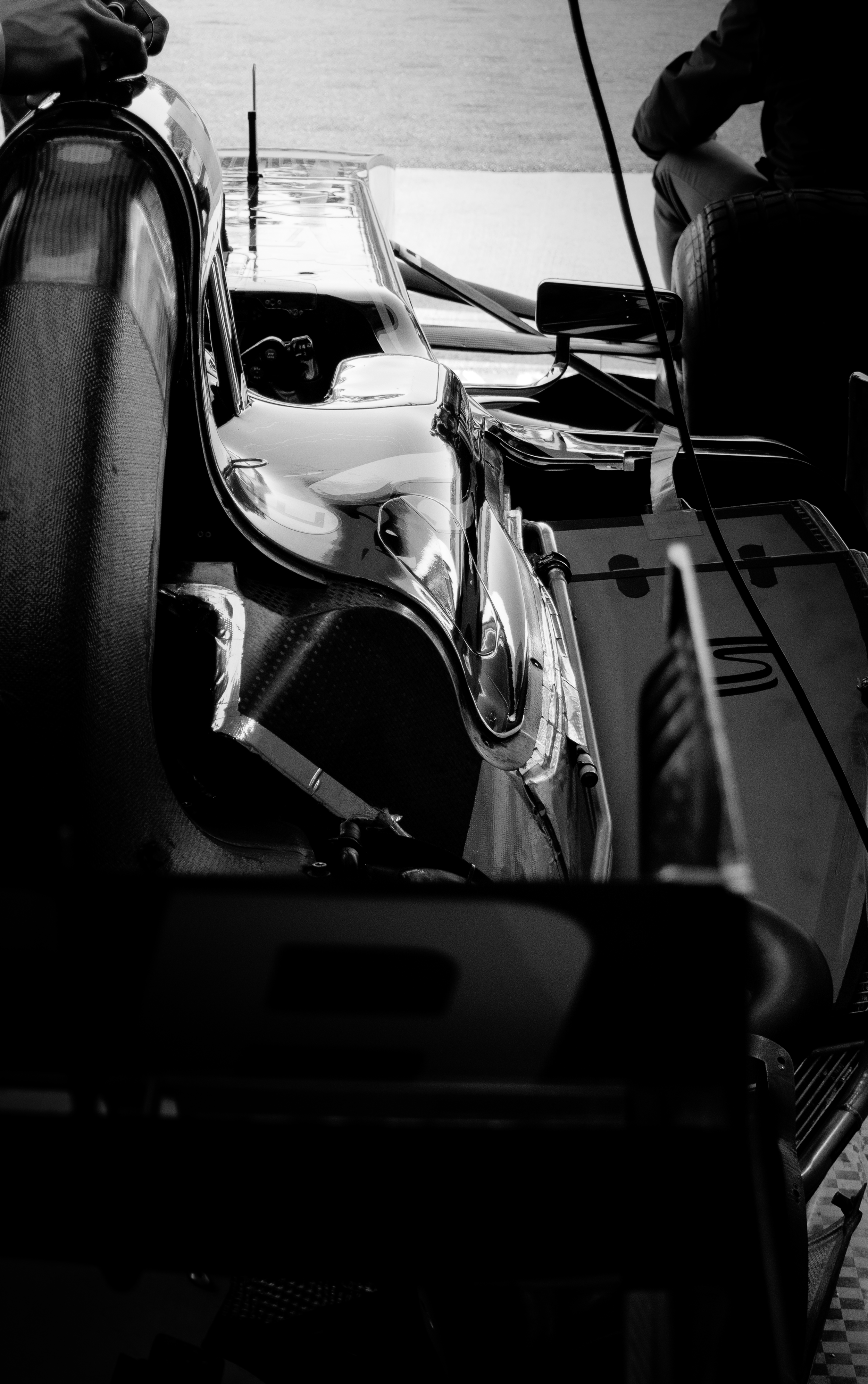 Voiture de course dans un stand de garage, avec un homme assis à côté, dans un environnement de course automobile.