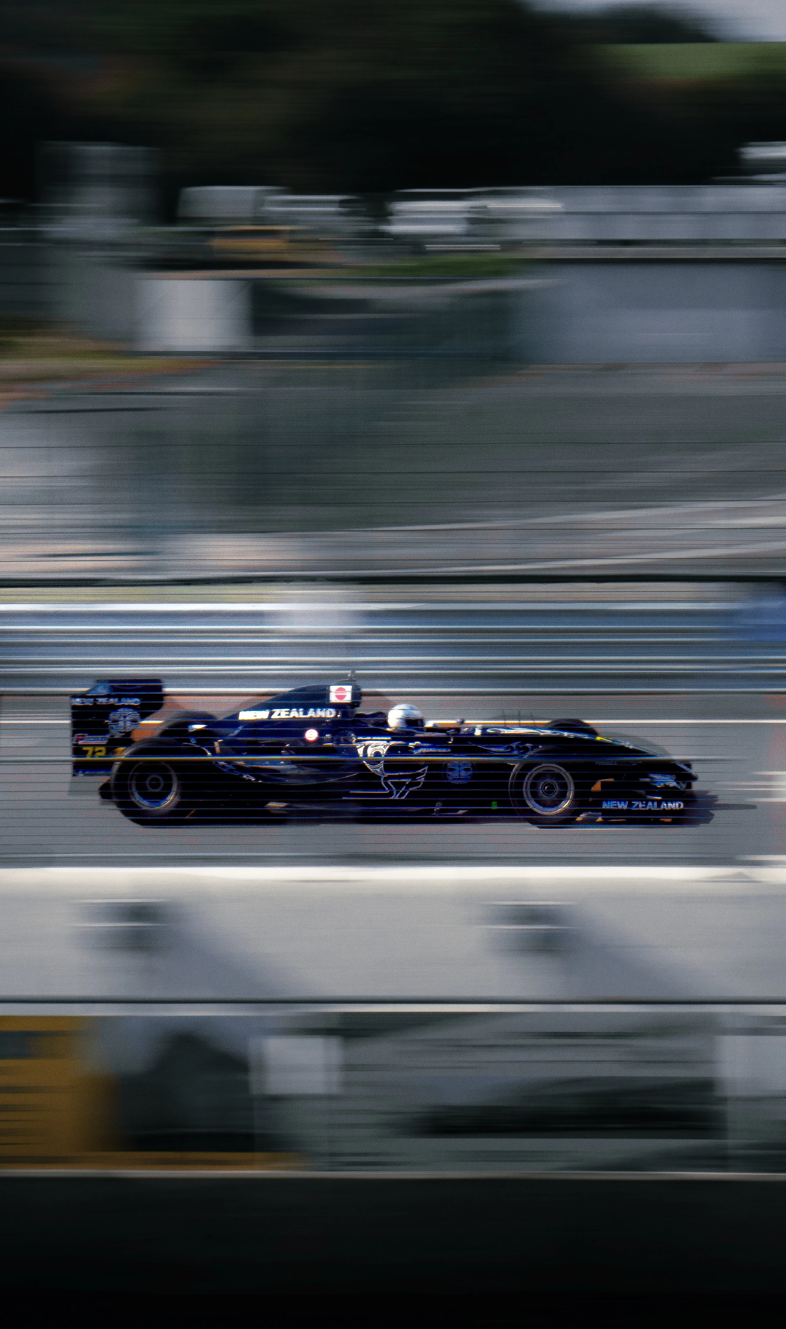 Voiture de course de type Formule 1 en mouvement sur une piste, avec un design bleu et des sponsors.